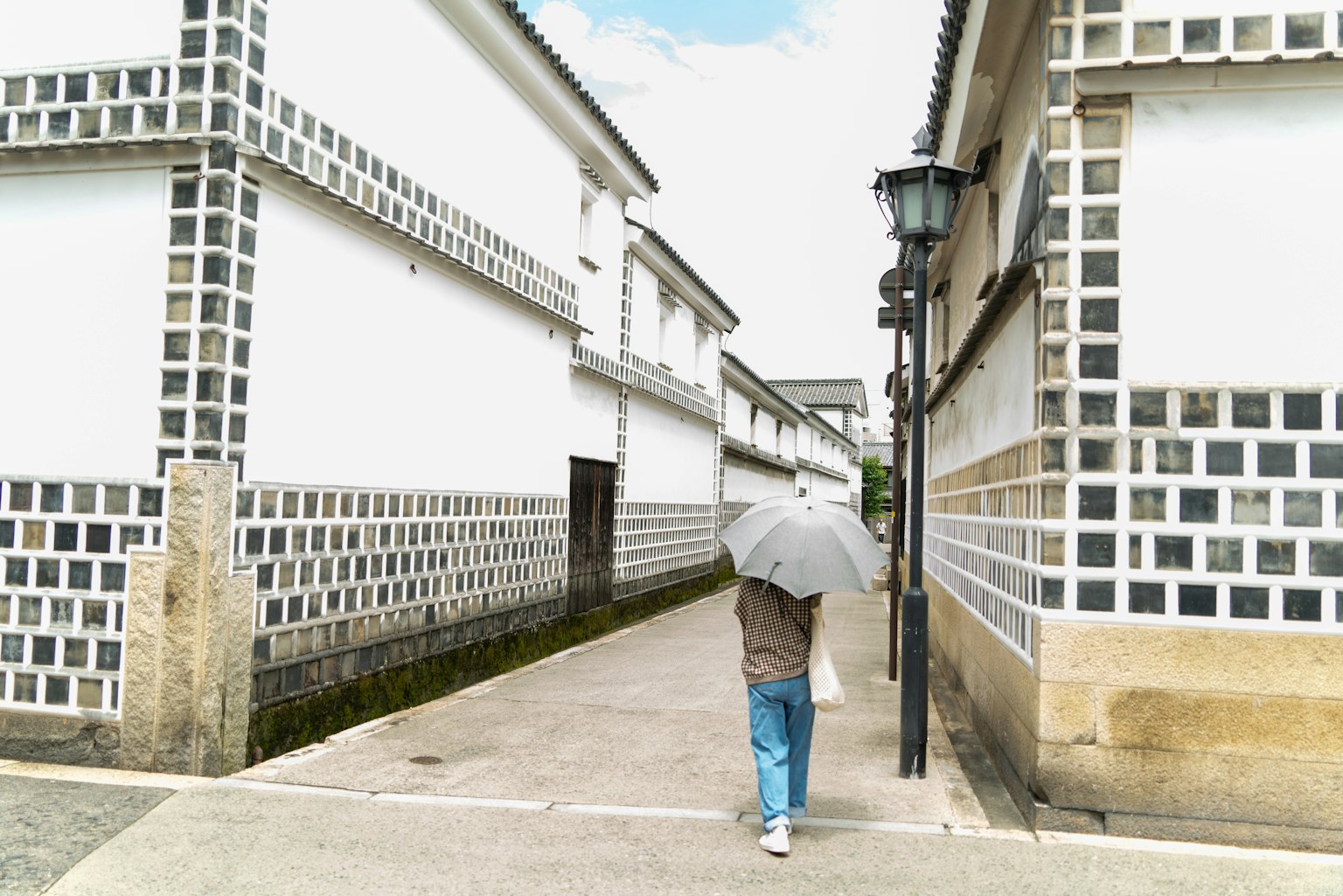 Une personne marchant avec un parapluie le long d'un chemin entre des bâtiments blancs avec des accents en carreaux noirs