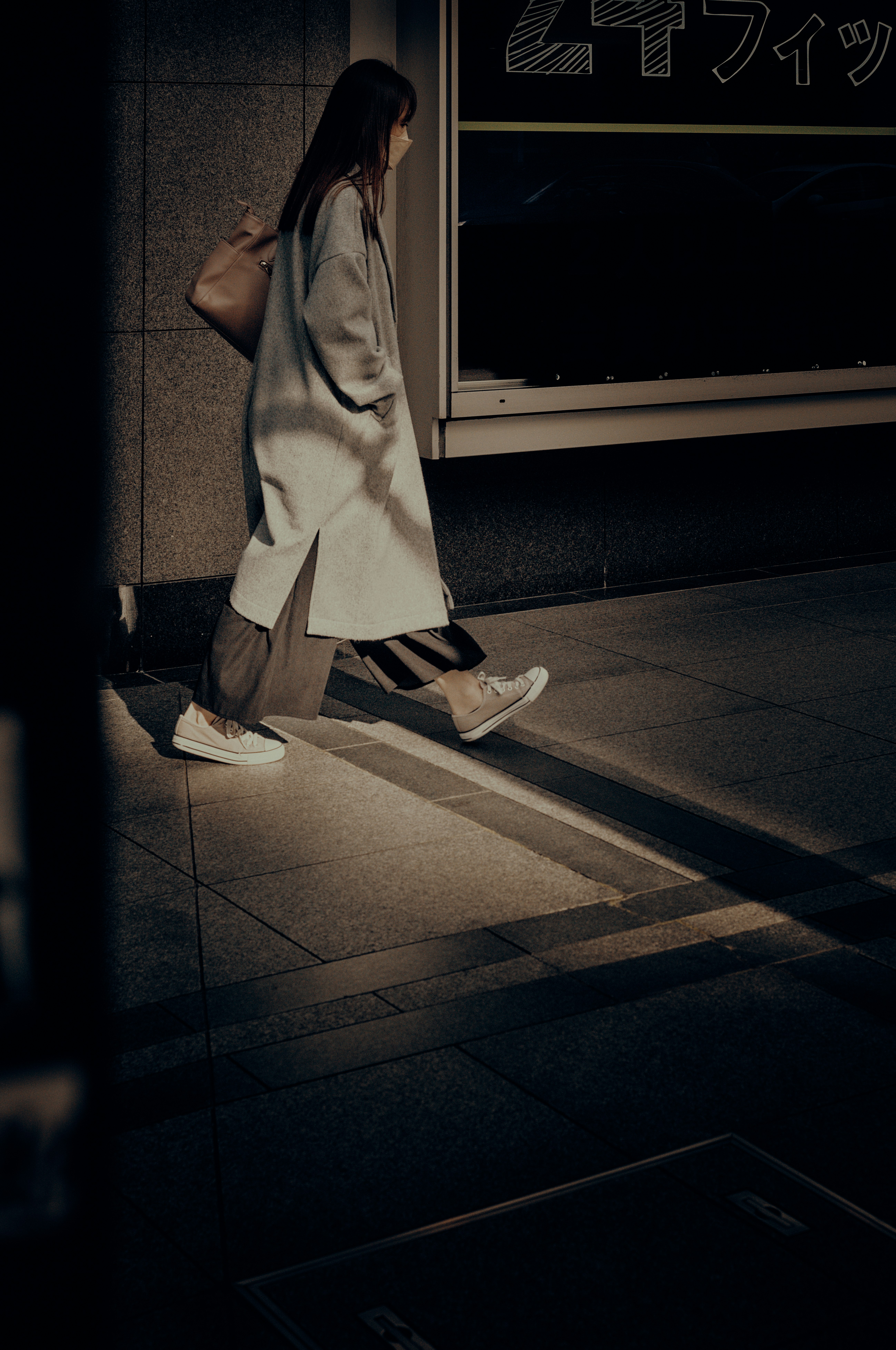 夜晚巷弄裡，手提購物袋的女性站在店鋪燈光下