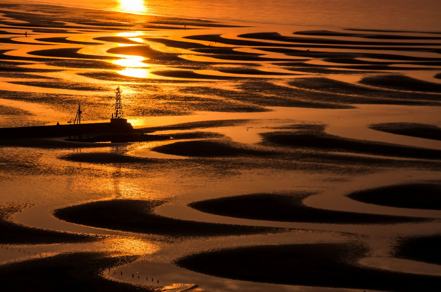 Patrones de llanuras de mareas reflejando el atardecer con un faro