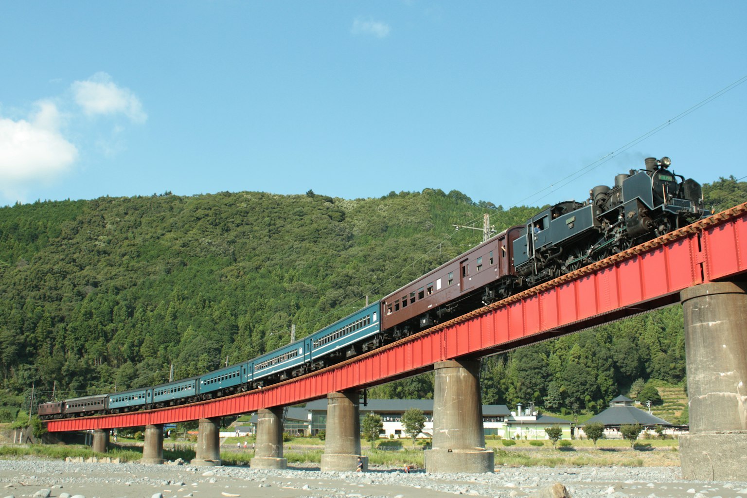 Locomotora de vapor cruzando un puente rojo con vagones de pasajeros