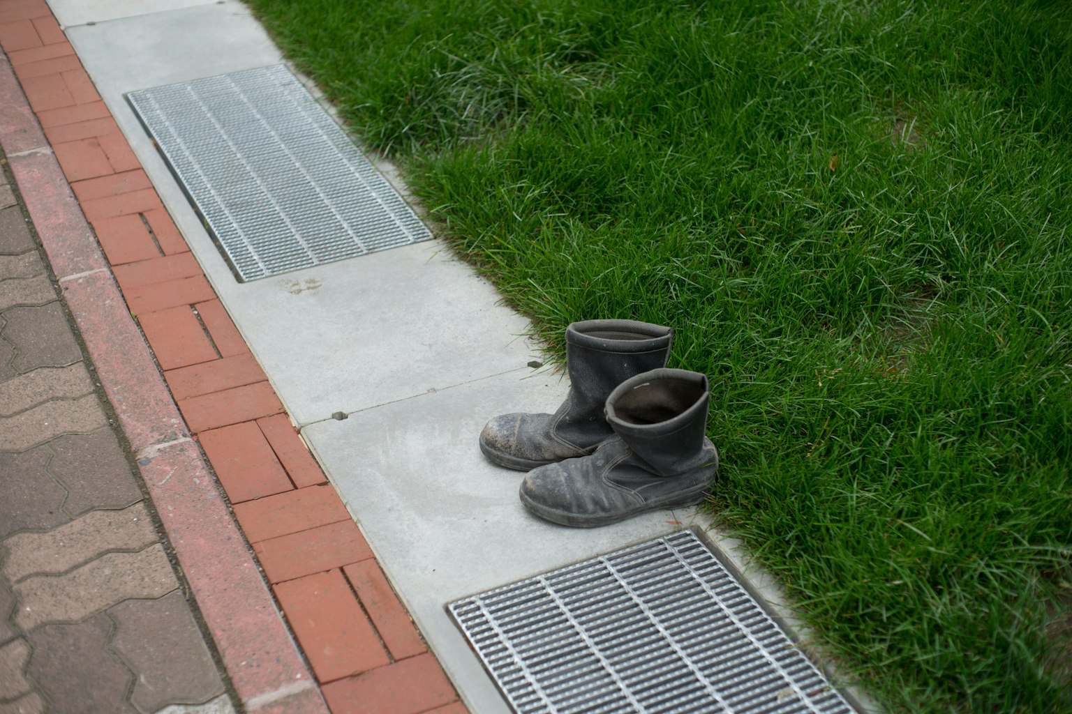 Schmutzige Stiefel auf Gras neben einem gepflasterten Weg