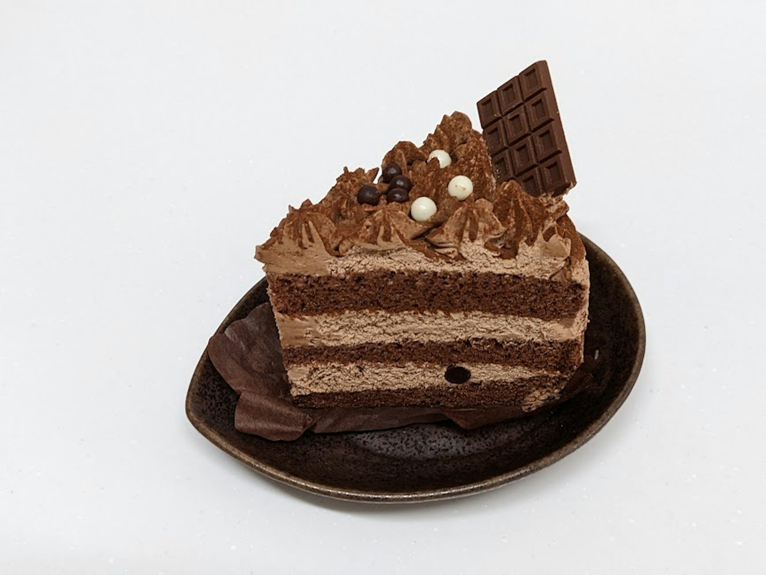 Une part de gâteau au chocolat avec un glaçage au chocolat crémeux et des couches de génoise décorées de morceaux de chocolat
