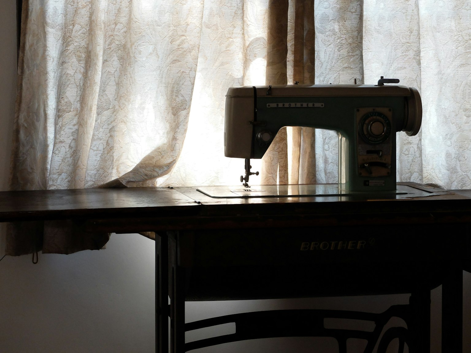 Una vecchia macchina da cucire vicino a una finestra con tende trasparenti