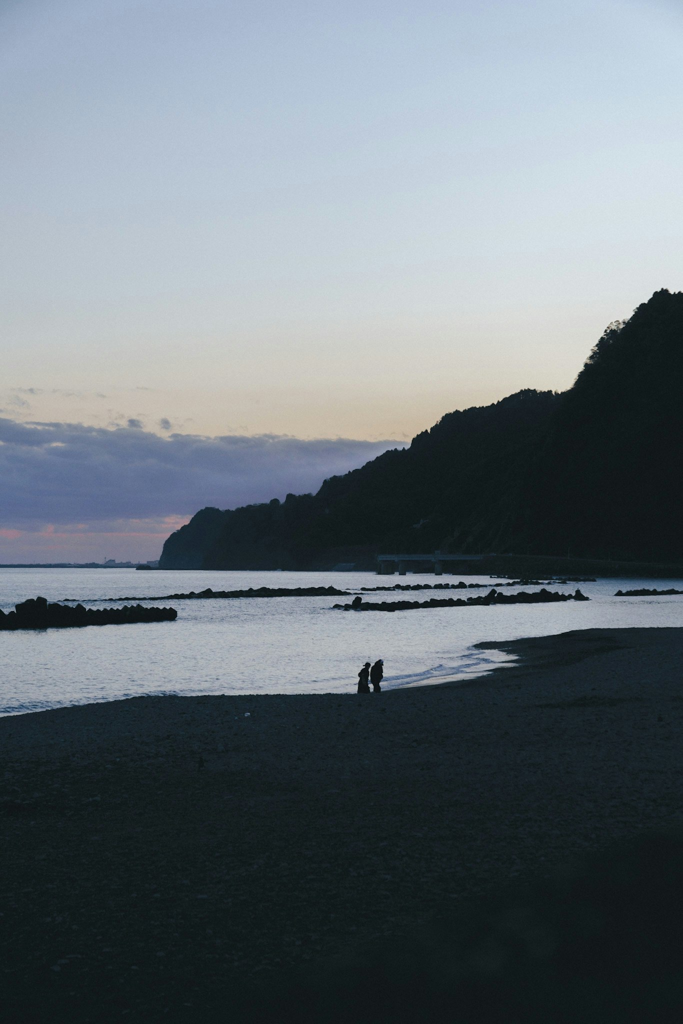 海辺の砂浜と夕日に染まる山の稜線
