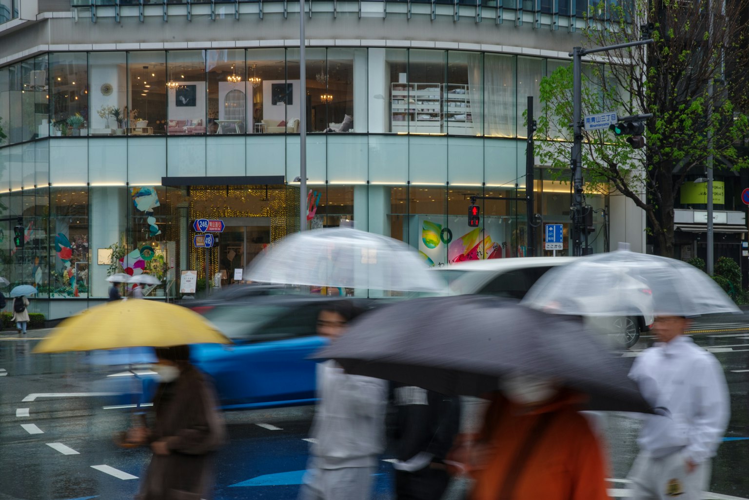 Des gens traversant la rue avec des parapluies sous la pluie et un bâtiment en verre