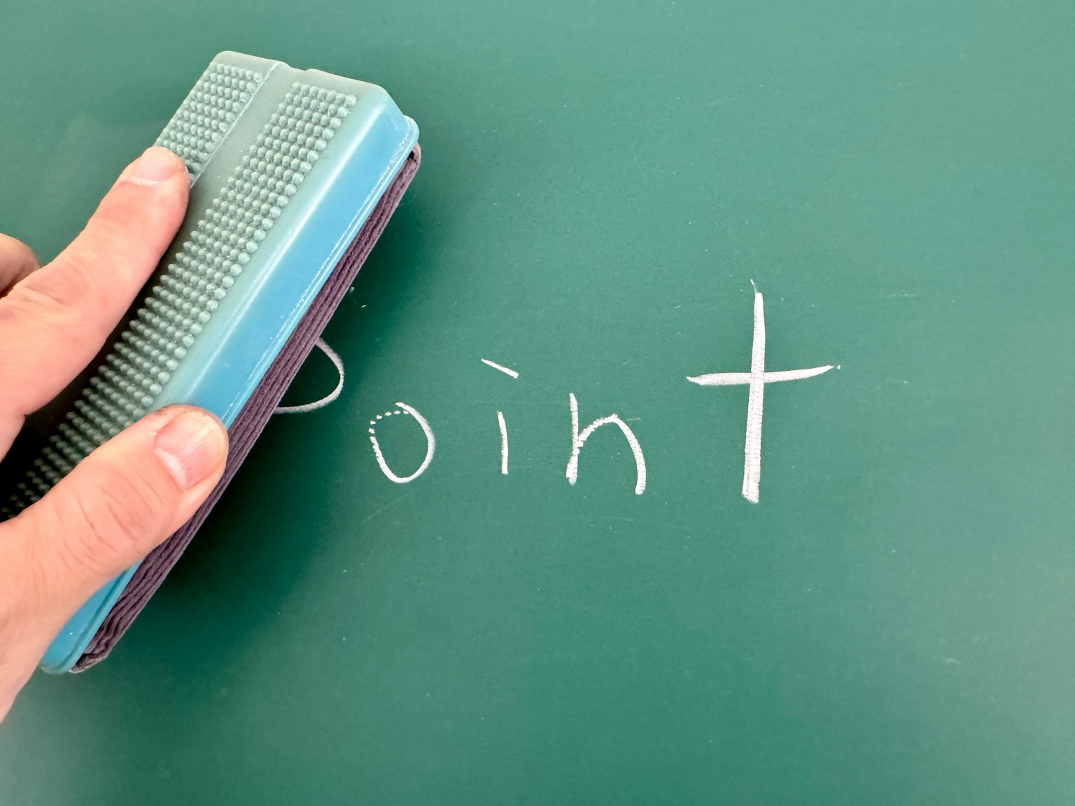 Tangan menghapus kata 'Point' yang ditulis dengan kapur putih di papan tulis hijau