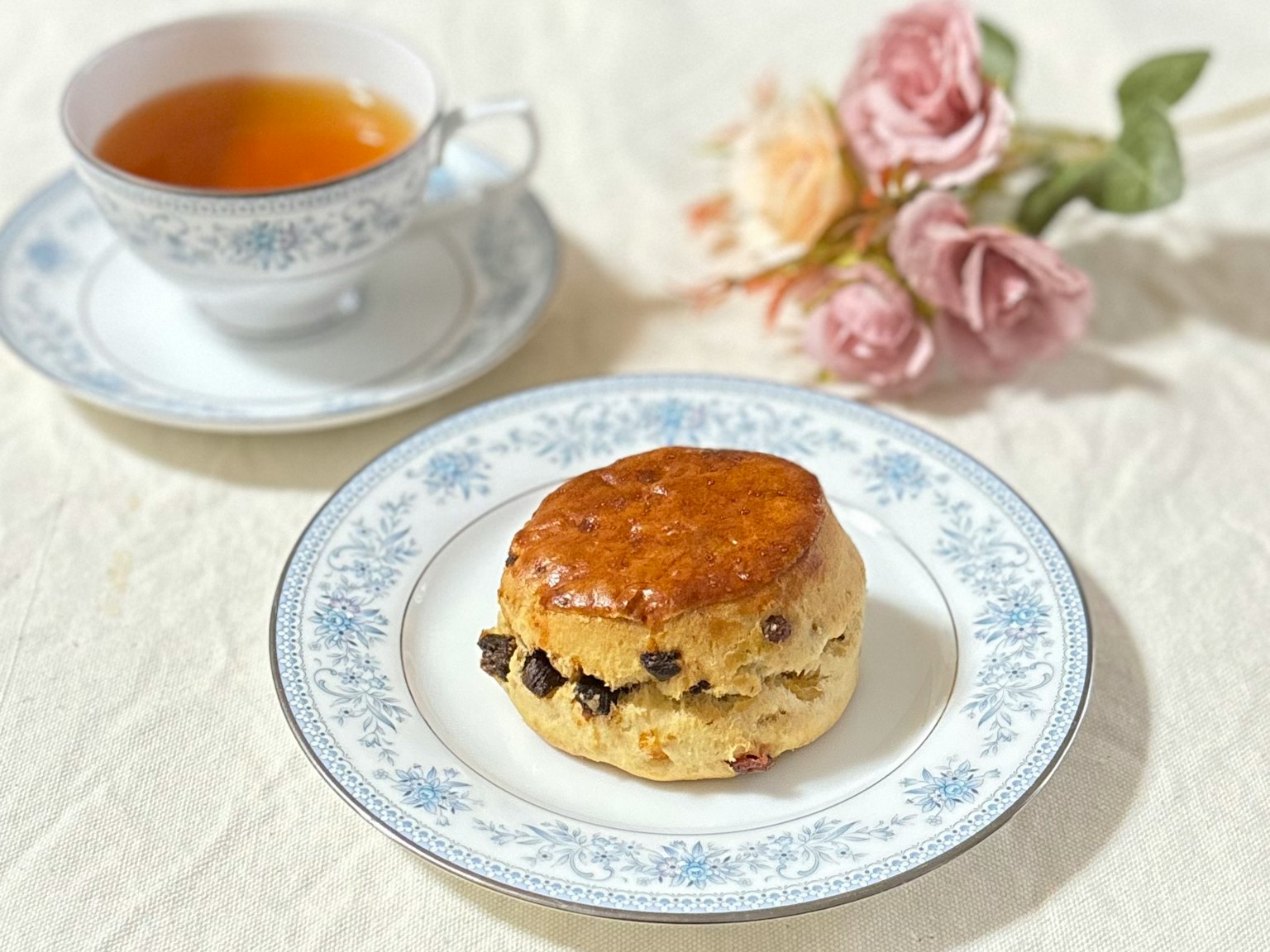 Un piatto con uno scone e una tazza di tè su un tavolo decorato con fiori