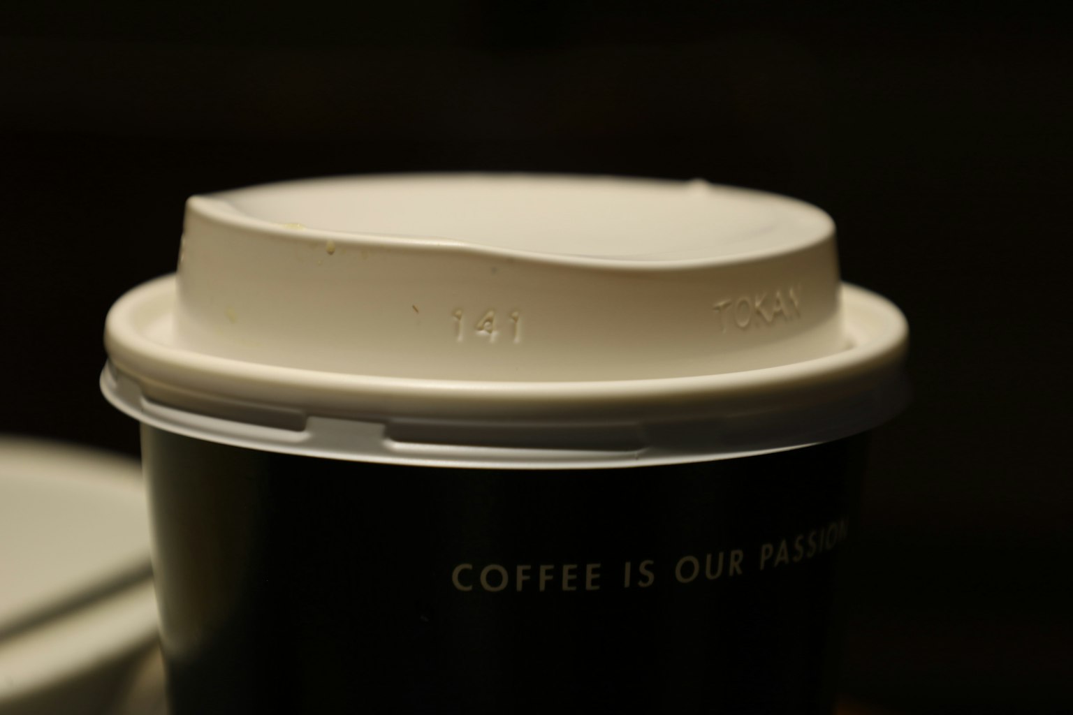 Primer plano de una tapa de taza de café con una taza negra que presenta el texto el café es nuestra pasión