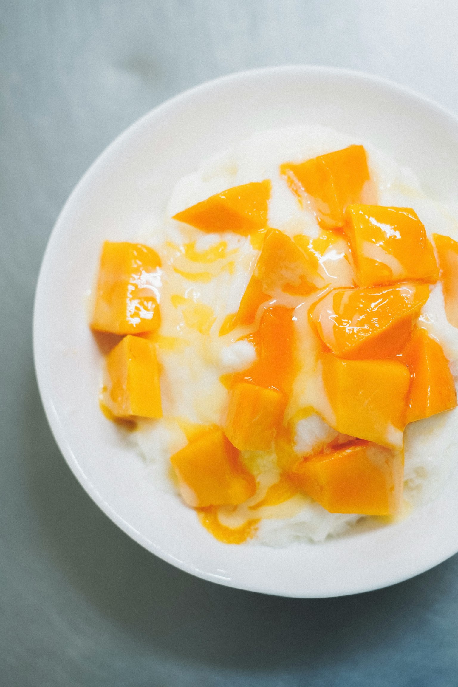 A dessert of mango chunks on cream in a white bowl