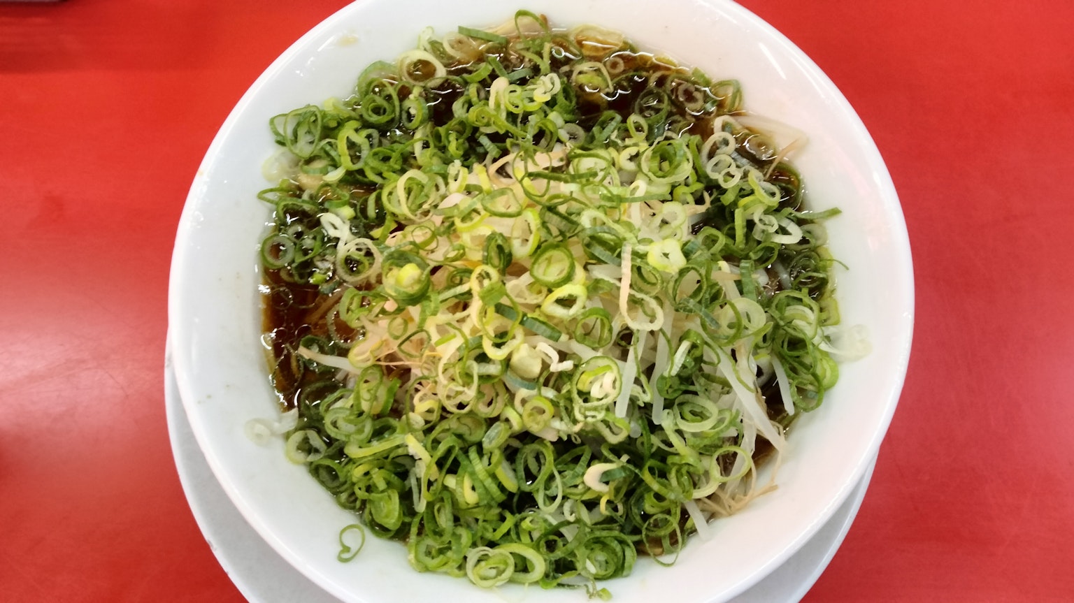 Ciotola di ramen guarnita con cipollotti su un tavolo rosso