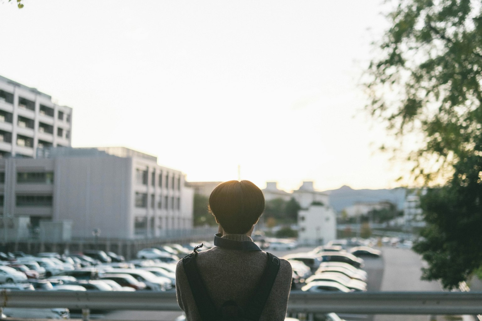 Une personne silhouettée contre le coucher de soleil surplombant un parking