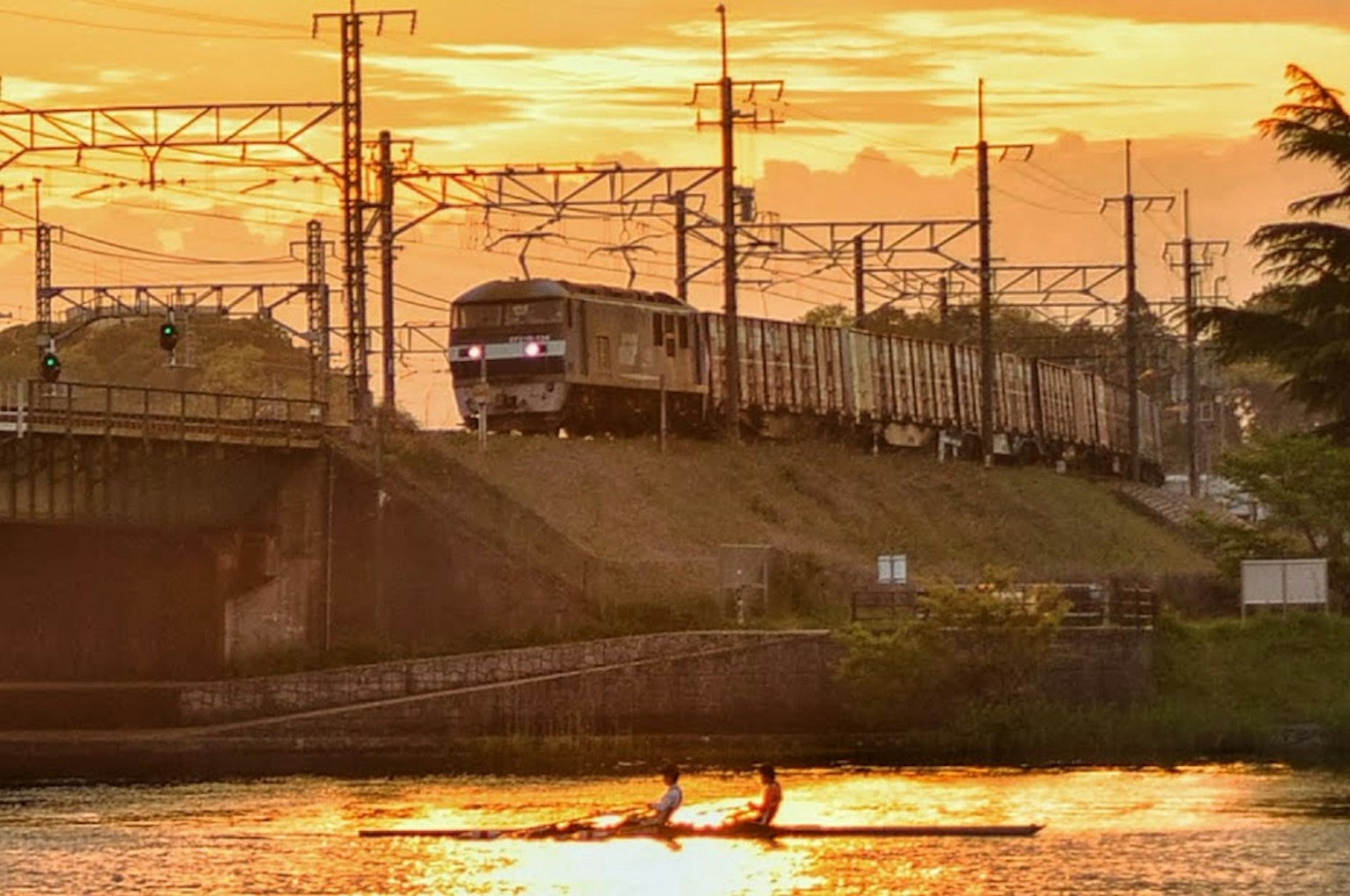 Treno merci che corre al tramonto con due canoisti sul fiume