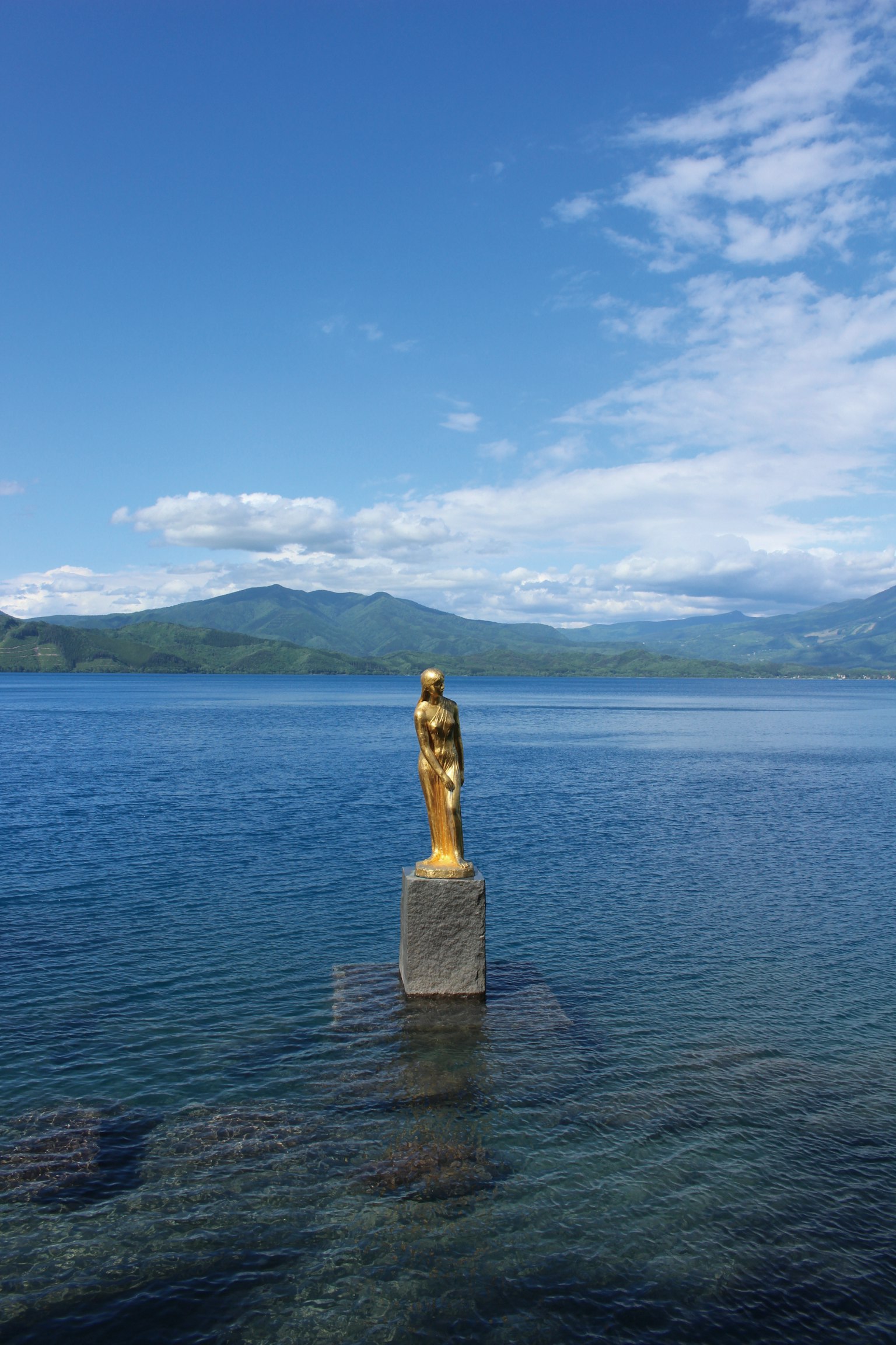 Estatua dorada de pie en el lago con cielo azul y montañas al fondo