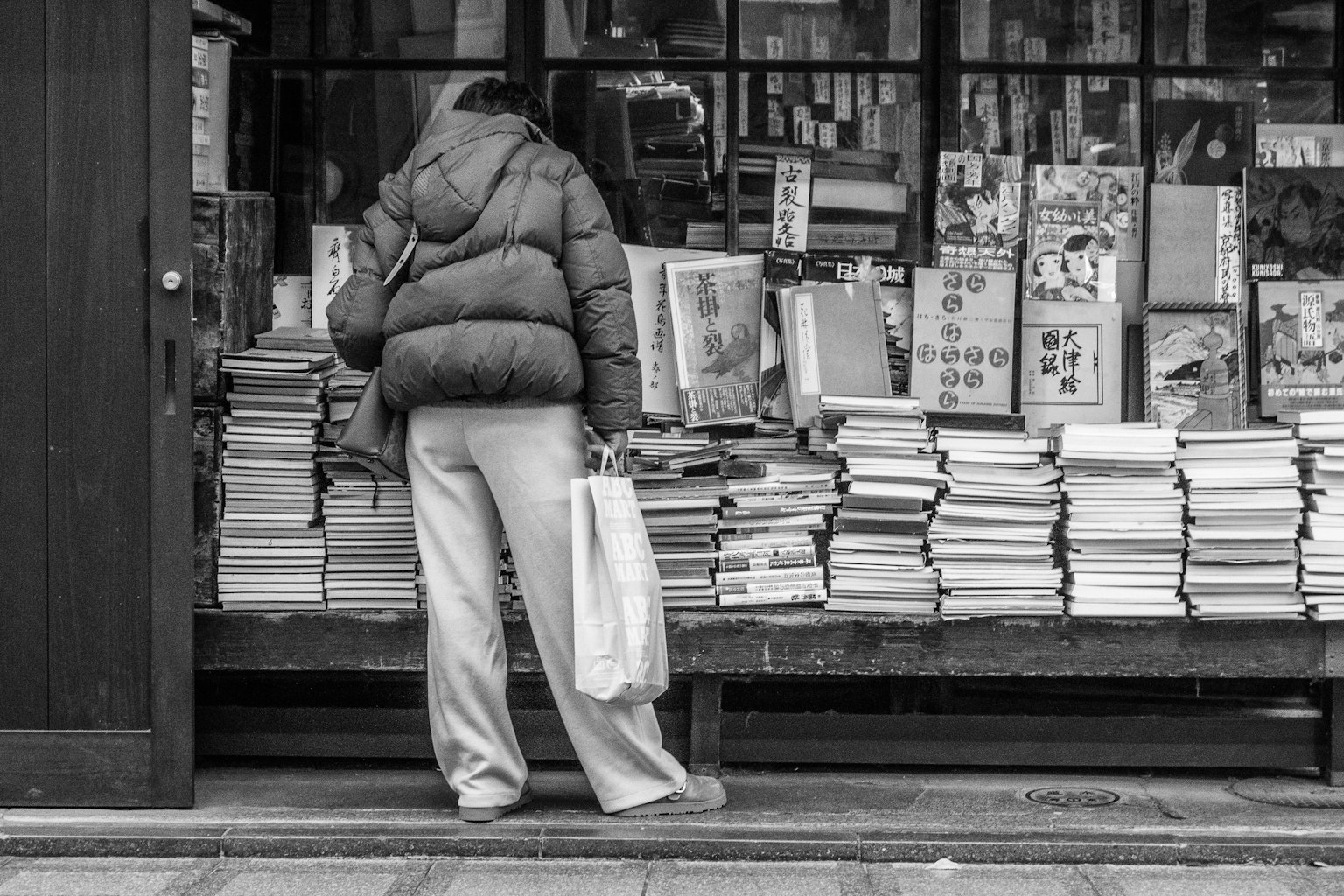 Person steht vor einem Stapel Bücher in einem Schwarz-Weiß-Foto von einem Straßenbuchladen