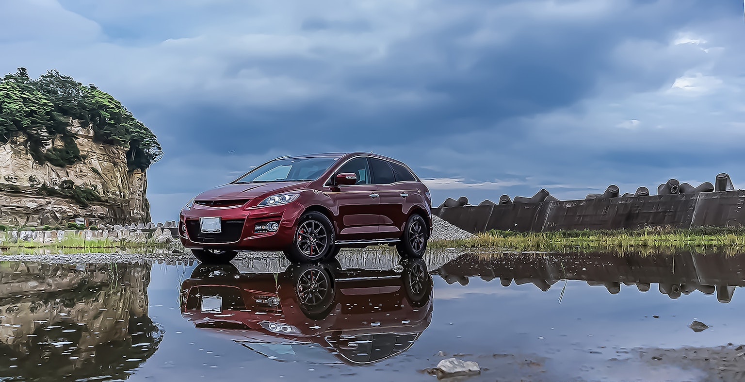 SUV rouge reflété dans une flaque avec des nuages dramatiques