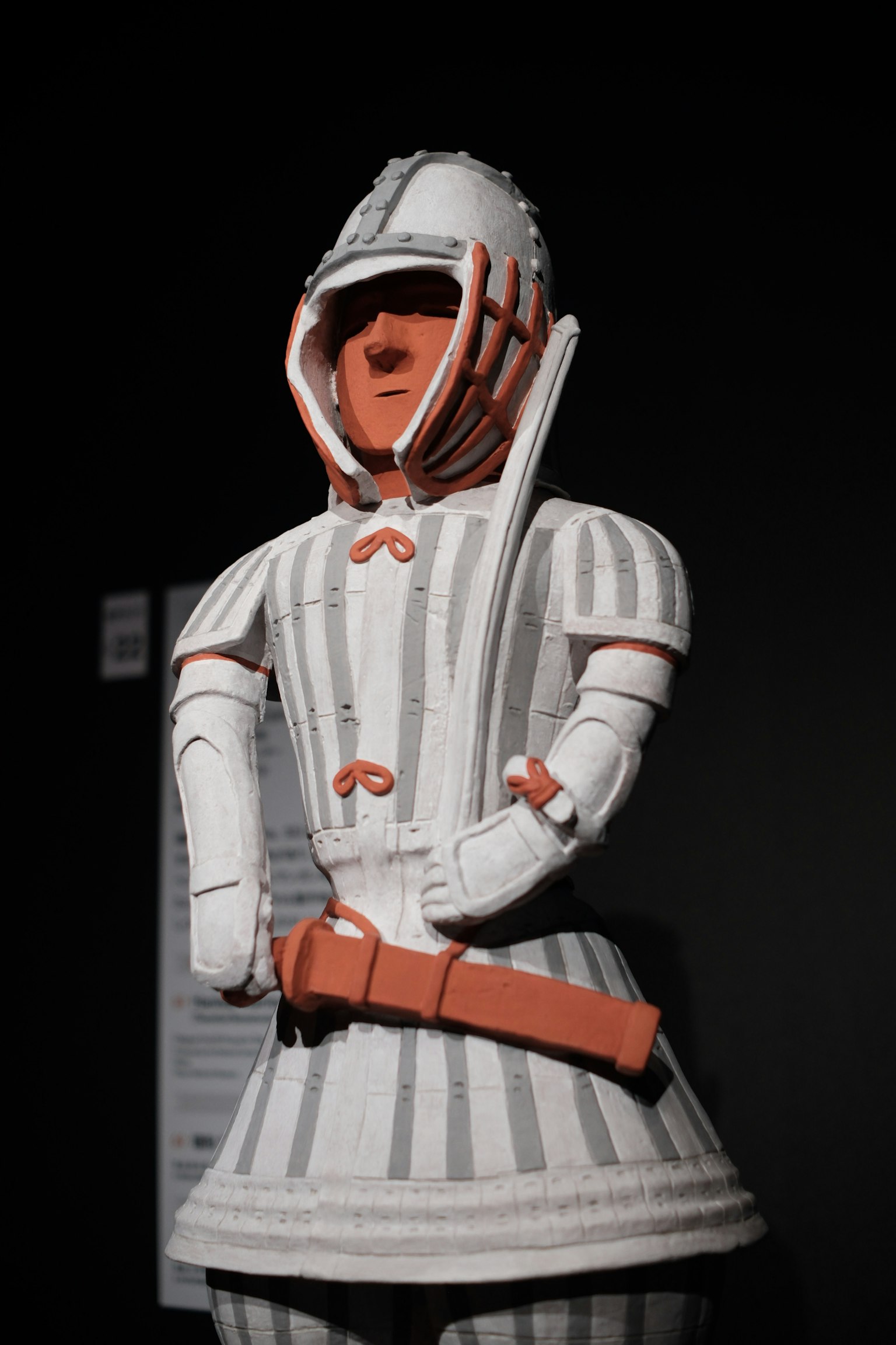 Eine Kriegerfigur mit weißen und orangefarbenen Verzierungen steht vor einem schwarzen Hintergrund