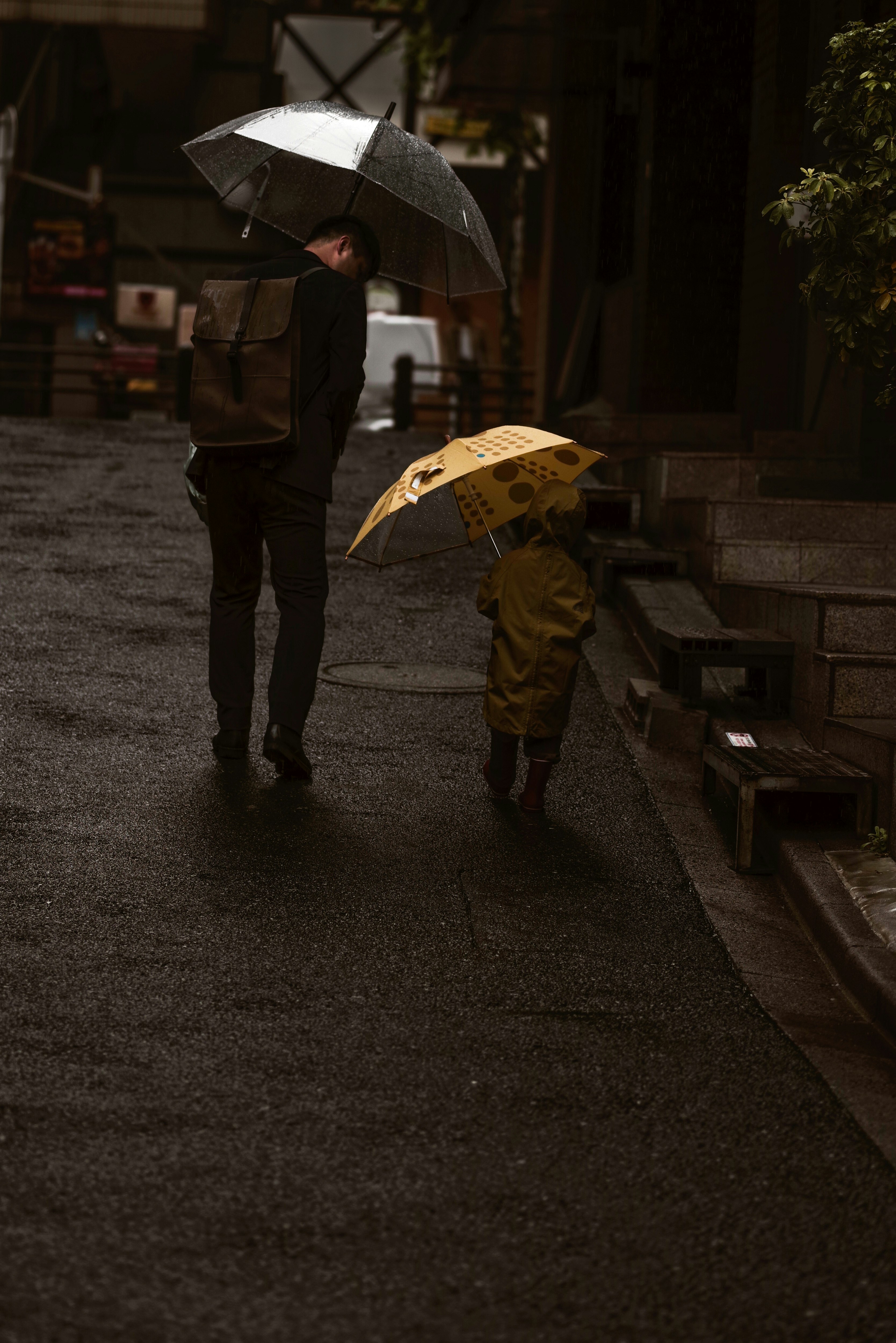 雨の朝の傘をさす親子の街並み