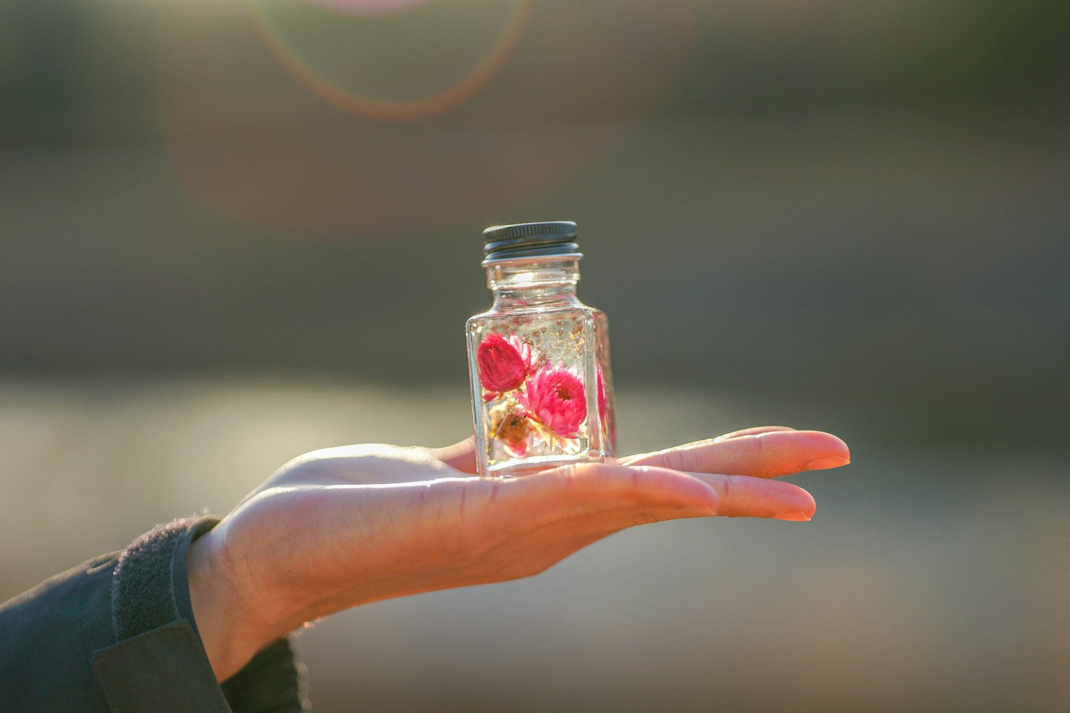 一隻開放的手中拿著的小玻璃瓶,裡面有粉紅色的花