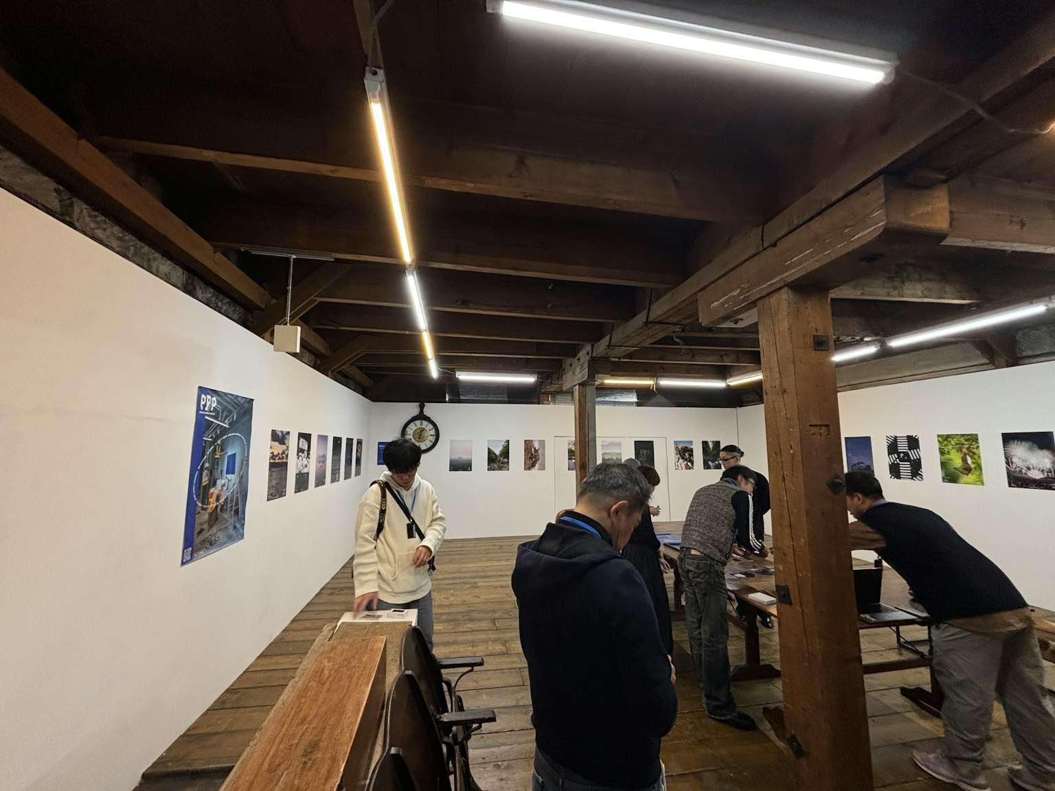 Interior galeri seni dengan balok kayu dan pencahayaan cerah menampilkan orang-orang yang melihat karya seni