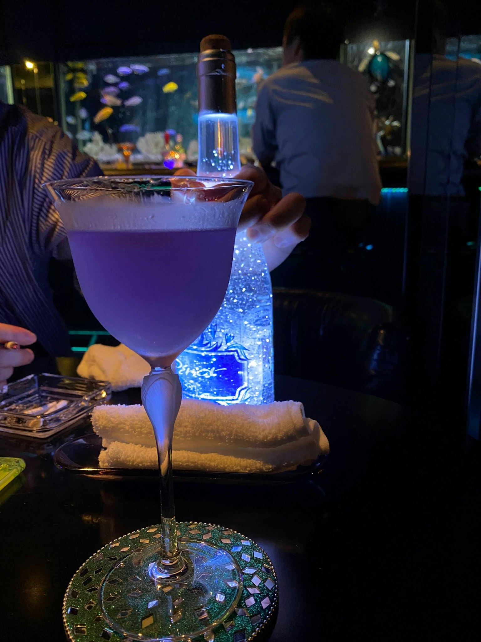 Cocktail viola su un tavolo con una bottiglia luminosa sullo sfondo
