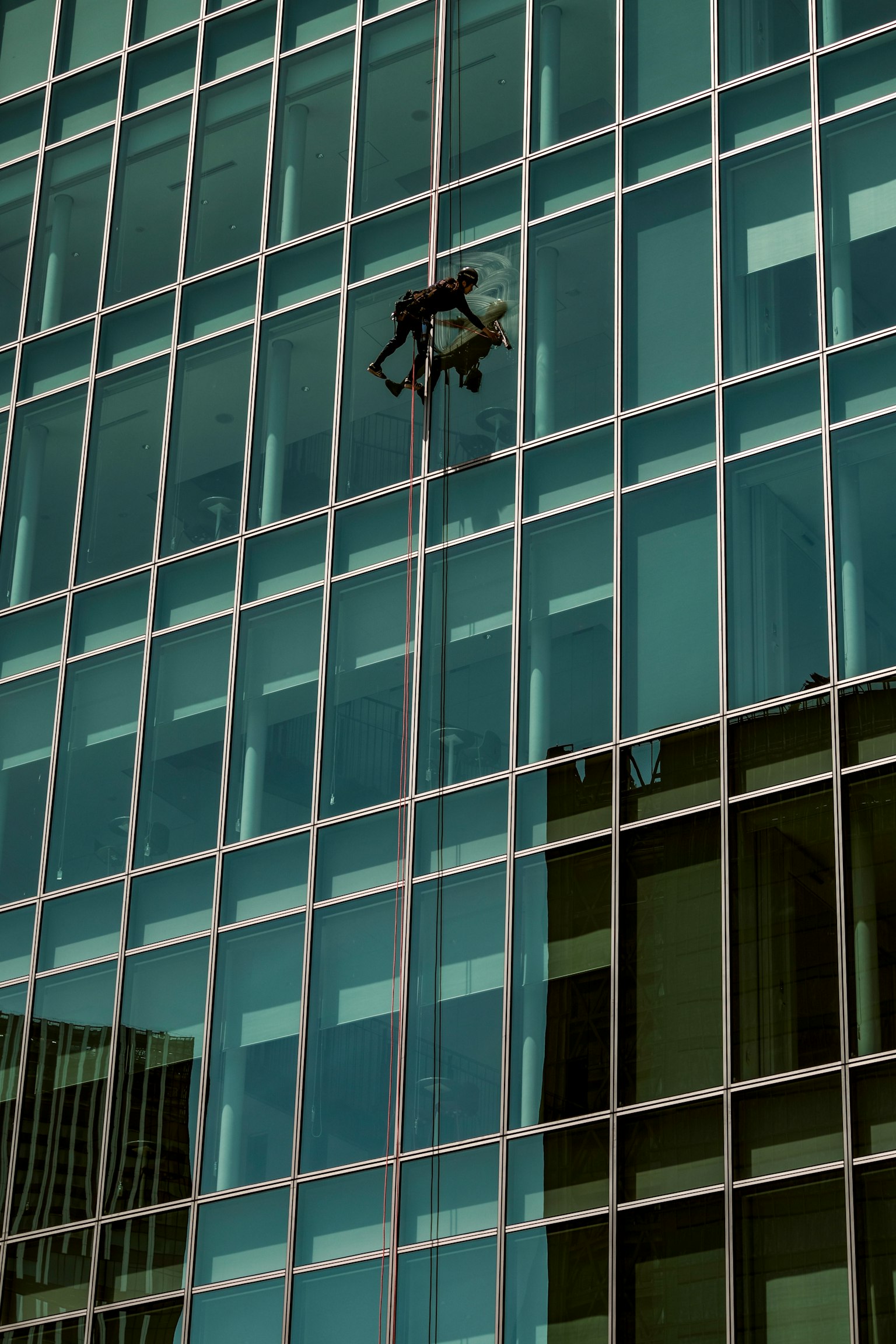 Person working on the exterior of a glass skyscraper