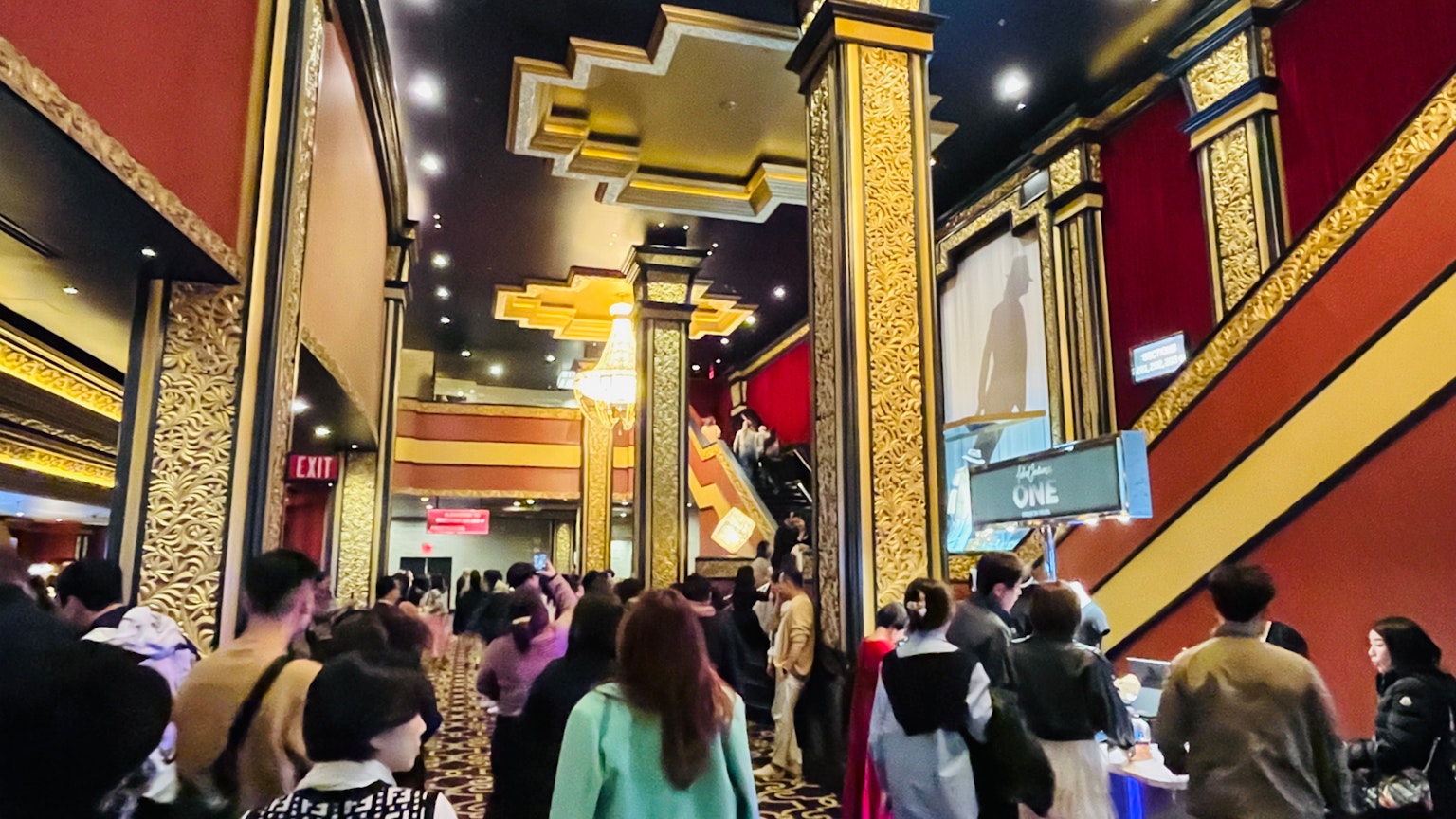 Lobby affollato di un teatro con decorazioni ornate e persone che scattano foto