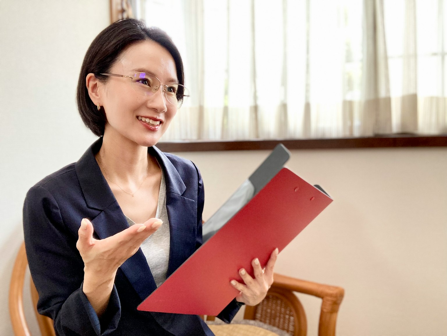 Seorang wanita tersenyum sambil memegang folder merah di dalam ruangan