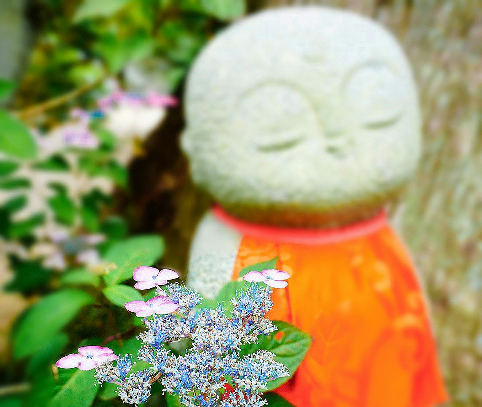Une statue en pierre avec les yeux fermés portant une robe orange entourée de fleurs