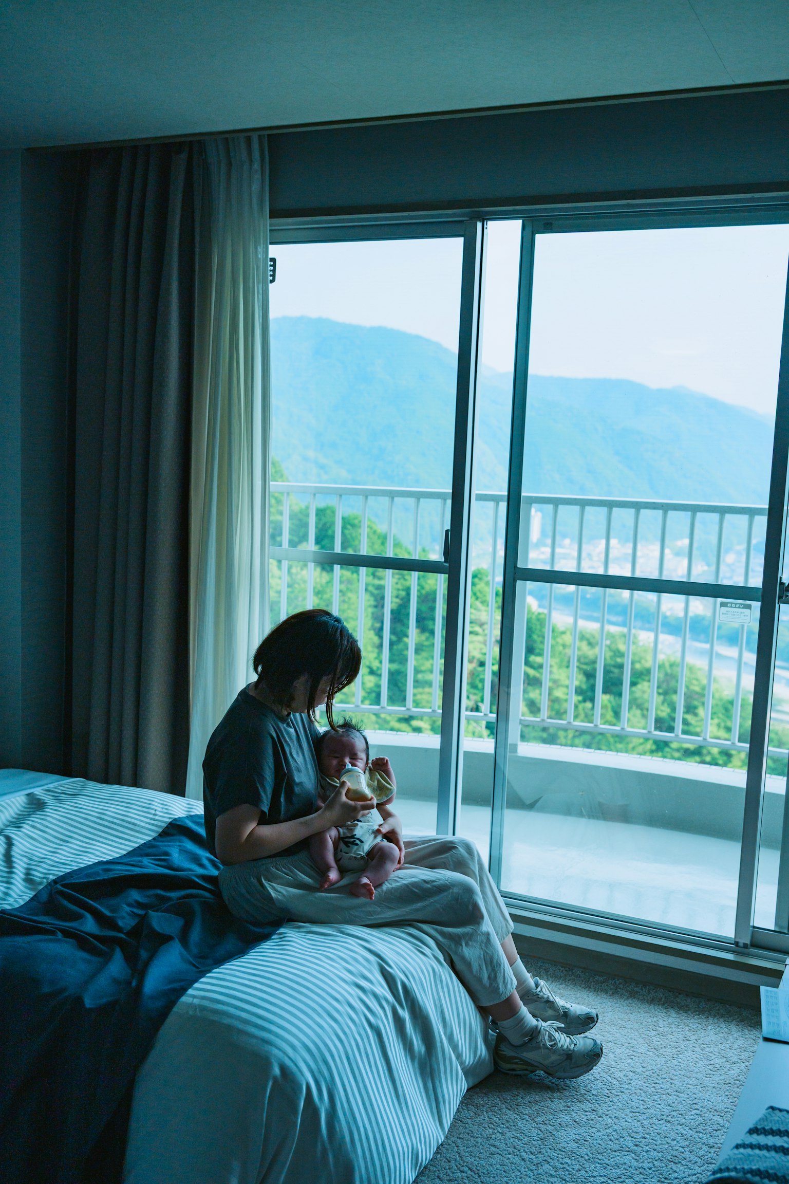 Một người phụ nữ ngồi bên cửa sổ ôm một con thú nhồi bông với cảnh núi