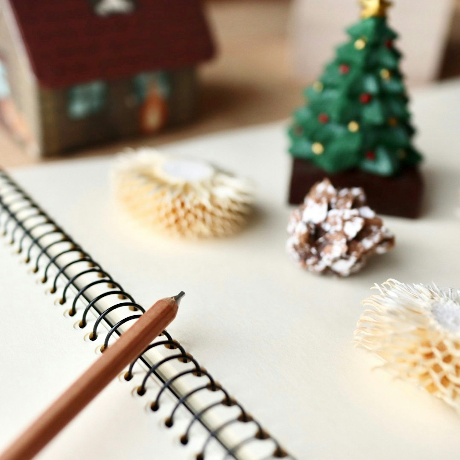 Une scène de bureau avec un sapin de Noël et une petite maison, un carnet et un crayon