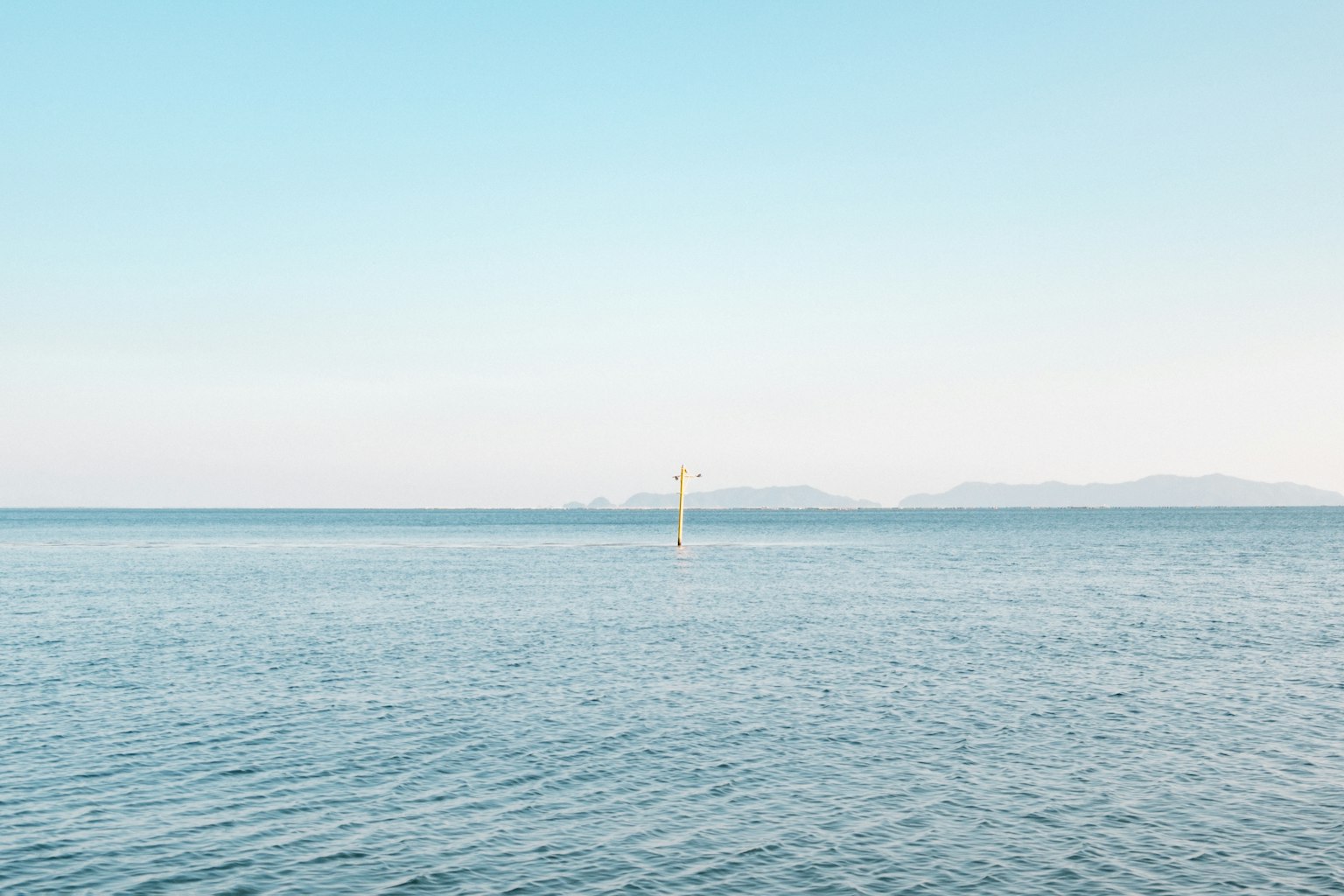 Paisaje de mar tranquilo y cielo azul con una pequeña isla a lo lejos