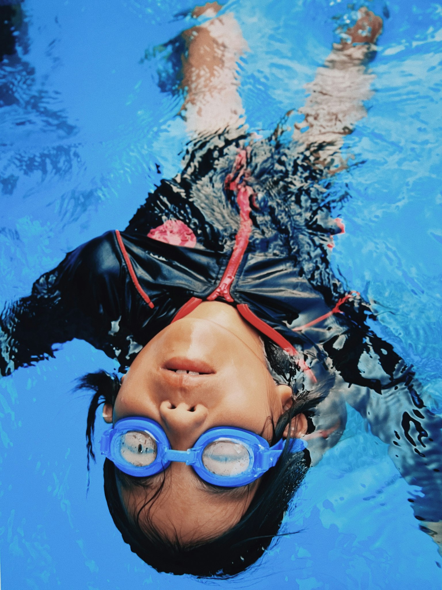 Child swimming underwater wearing blue goggles and a black swimsuit