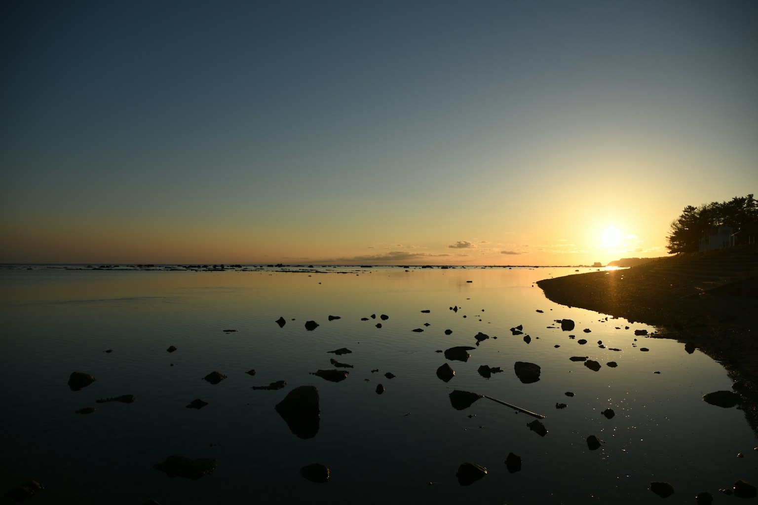 Ruhiger Strand mit Sonnenuntergang, der sich im Wasser und auf Steinen spiegelt
