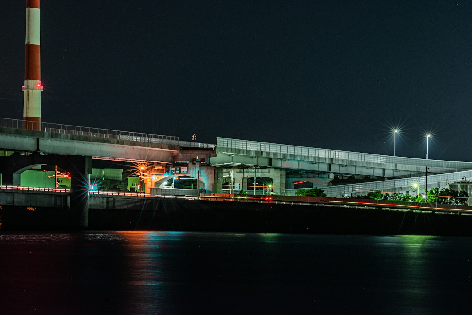 Vista nocturna de un área industrial con un puente y una chimenea