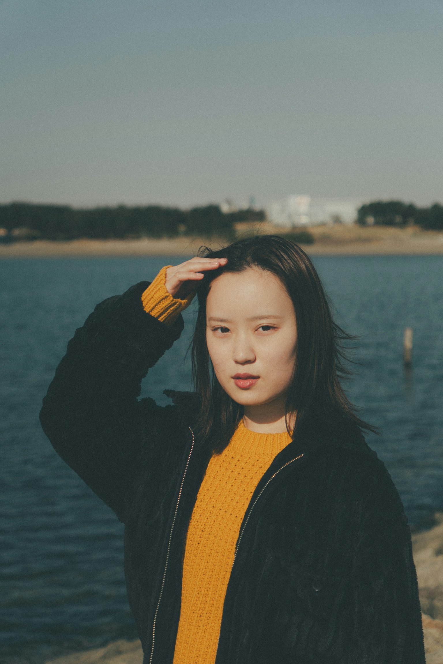 湖边站着的女性肖像，手放在头发上