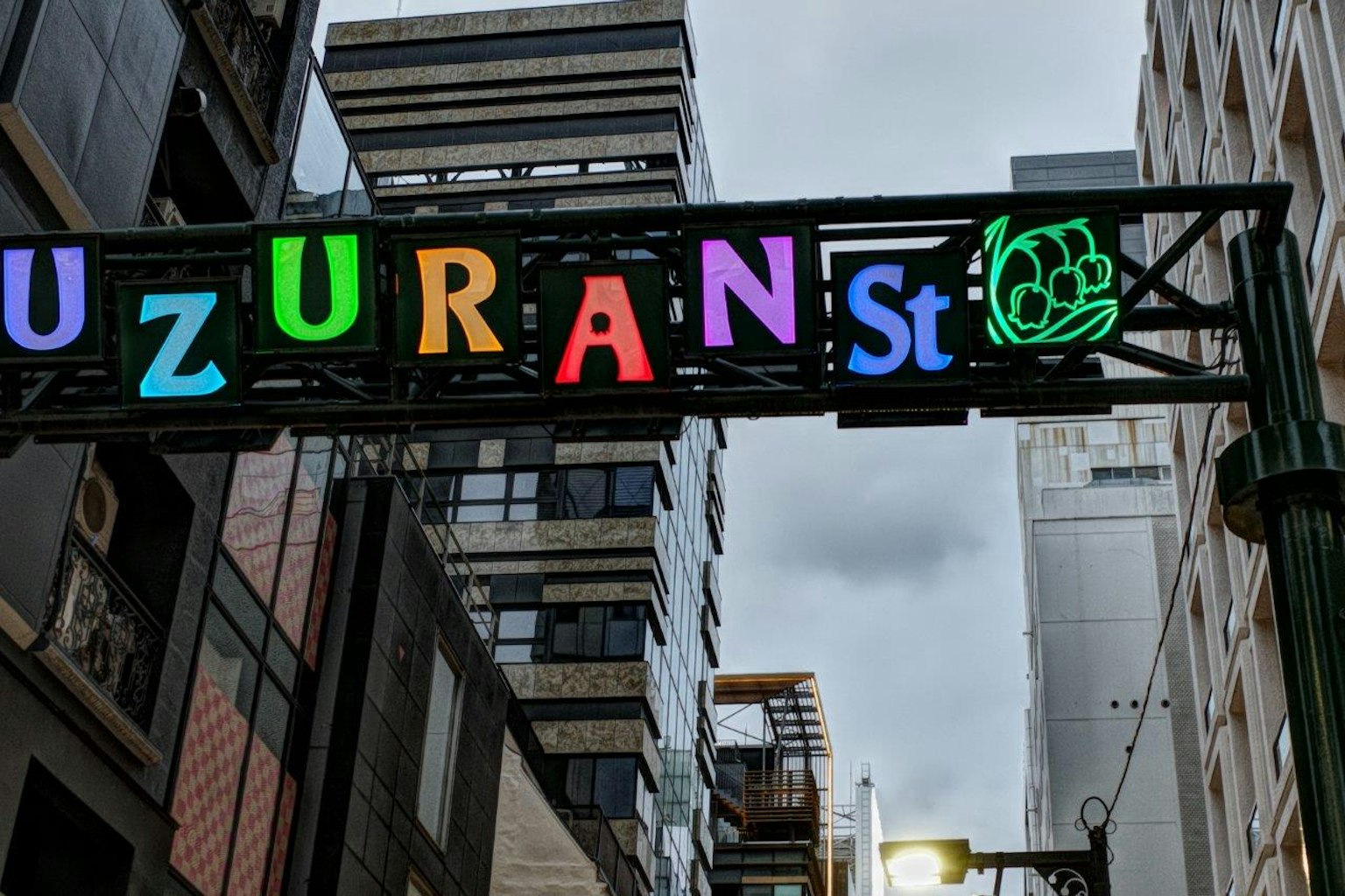 Buntes Schild mit der Aufschrift 'UZURAN St' in einer städtischen Umgebung