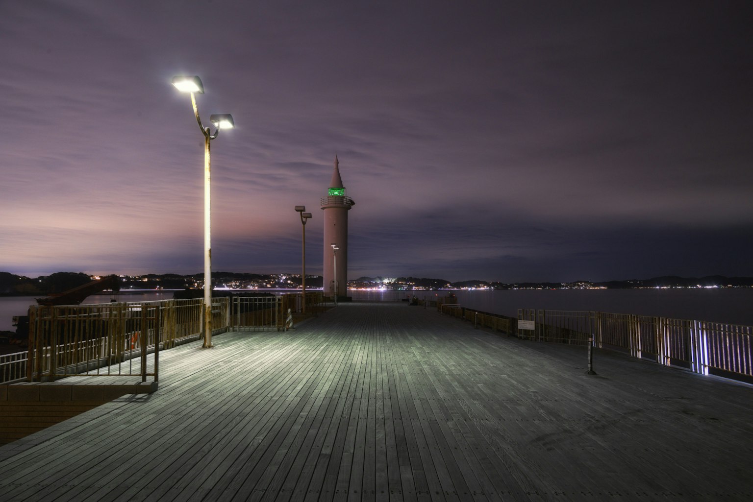 Vista notturna di un molo con un faro e lampioni