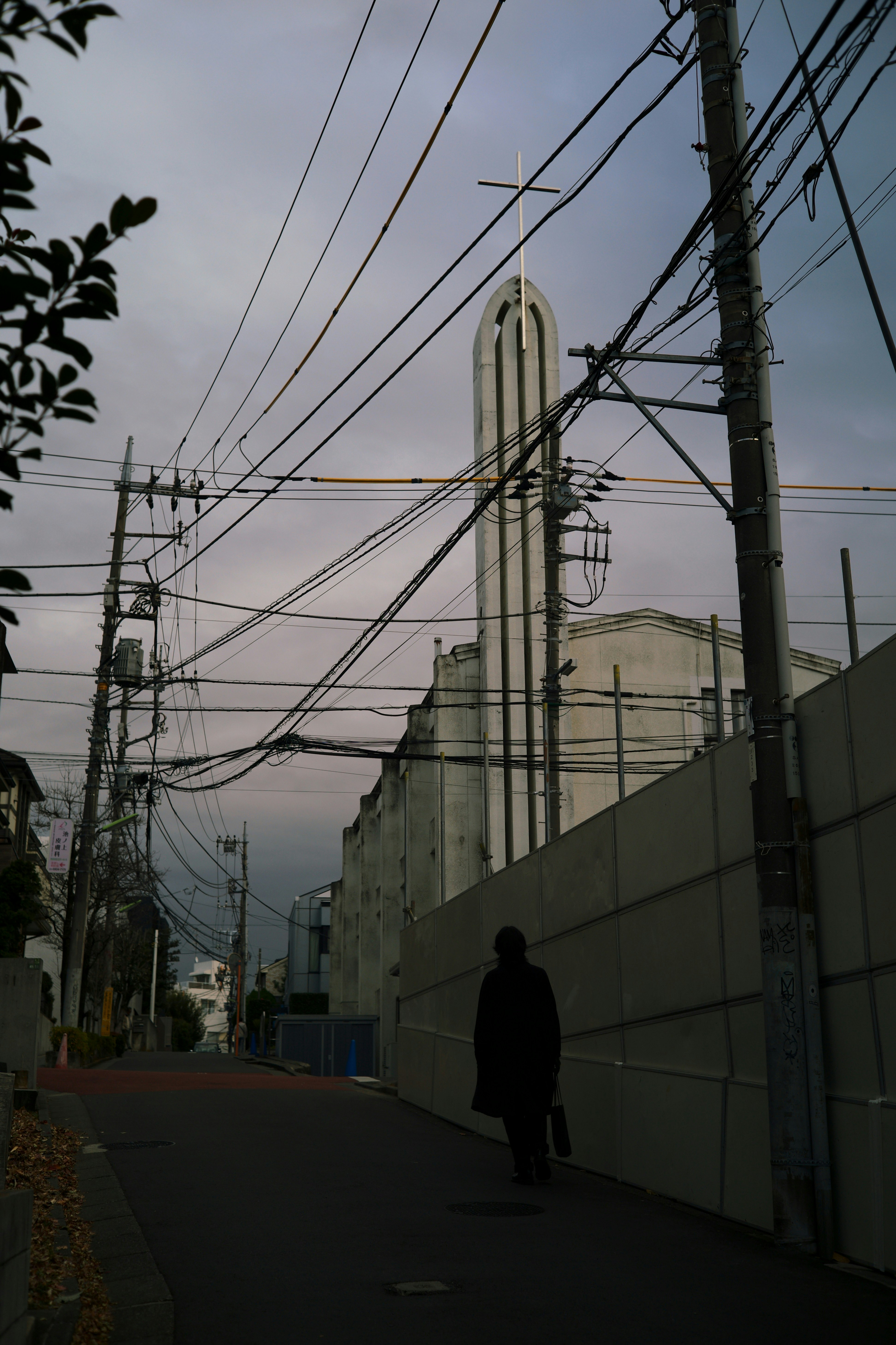 暗い空の下で電線が交差する街路を歩く人影と高い建物のシルエット