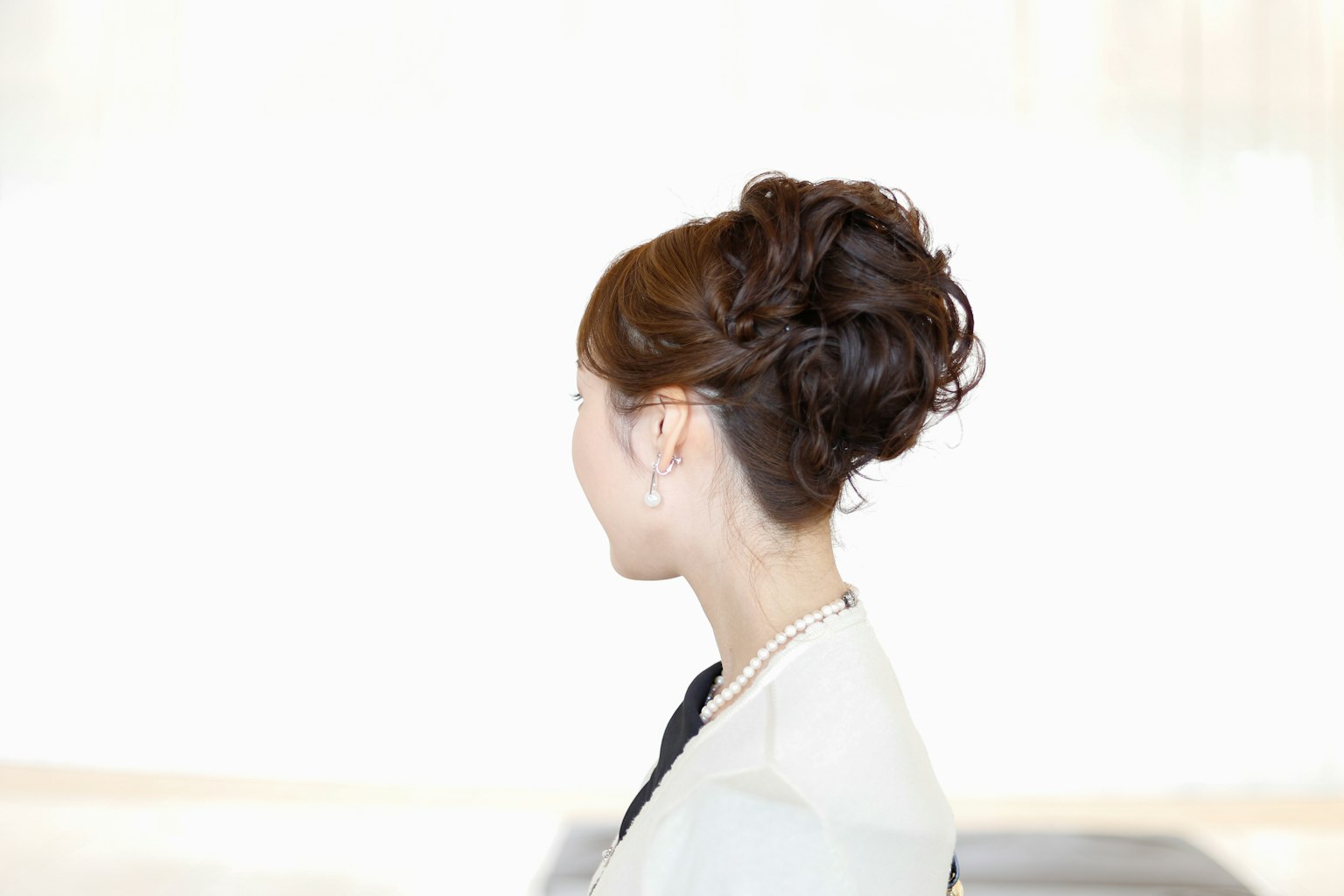 Femme vue de profil avec des cheveux bruns coiffés coiffure élégante tenue simple arrière-plan lumineux