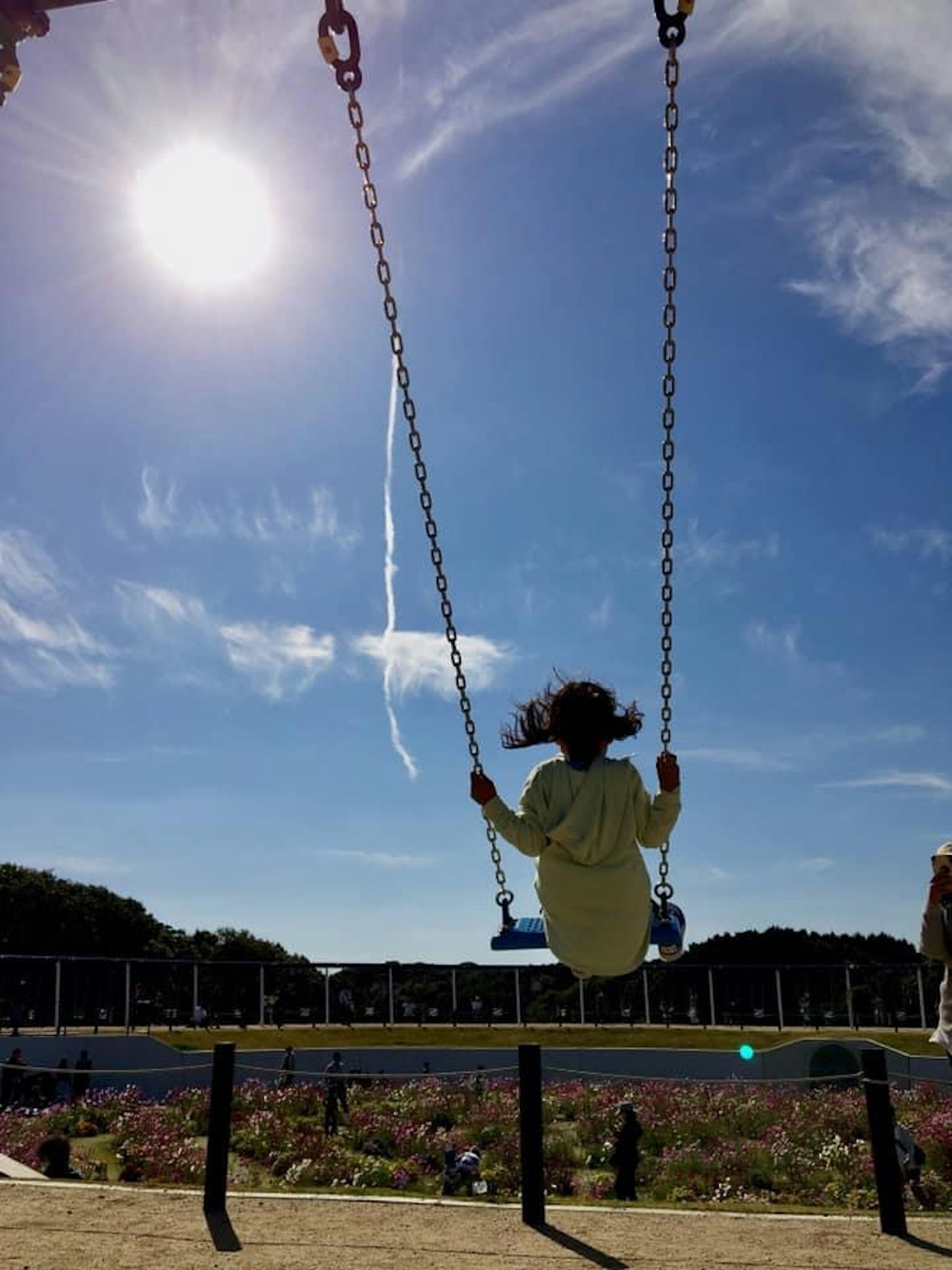 Silhouette d'un enfant sur une balançoire dans un parc avec un soleil brillant