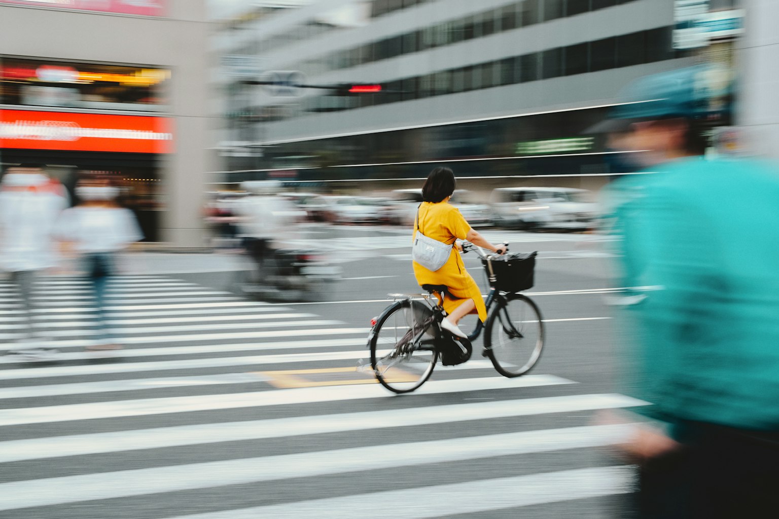 A woman in a yellow outfit riding a bicycle across a crosswalk in a city scene