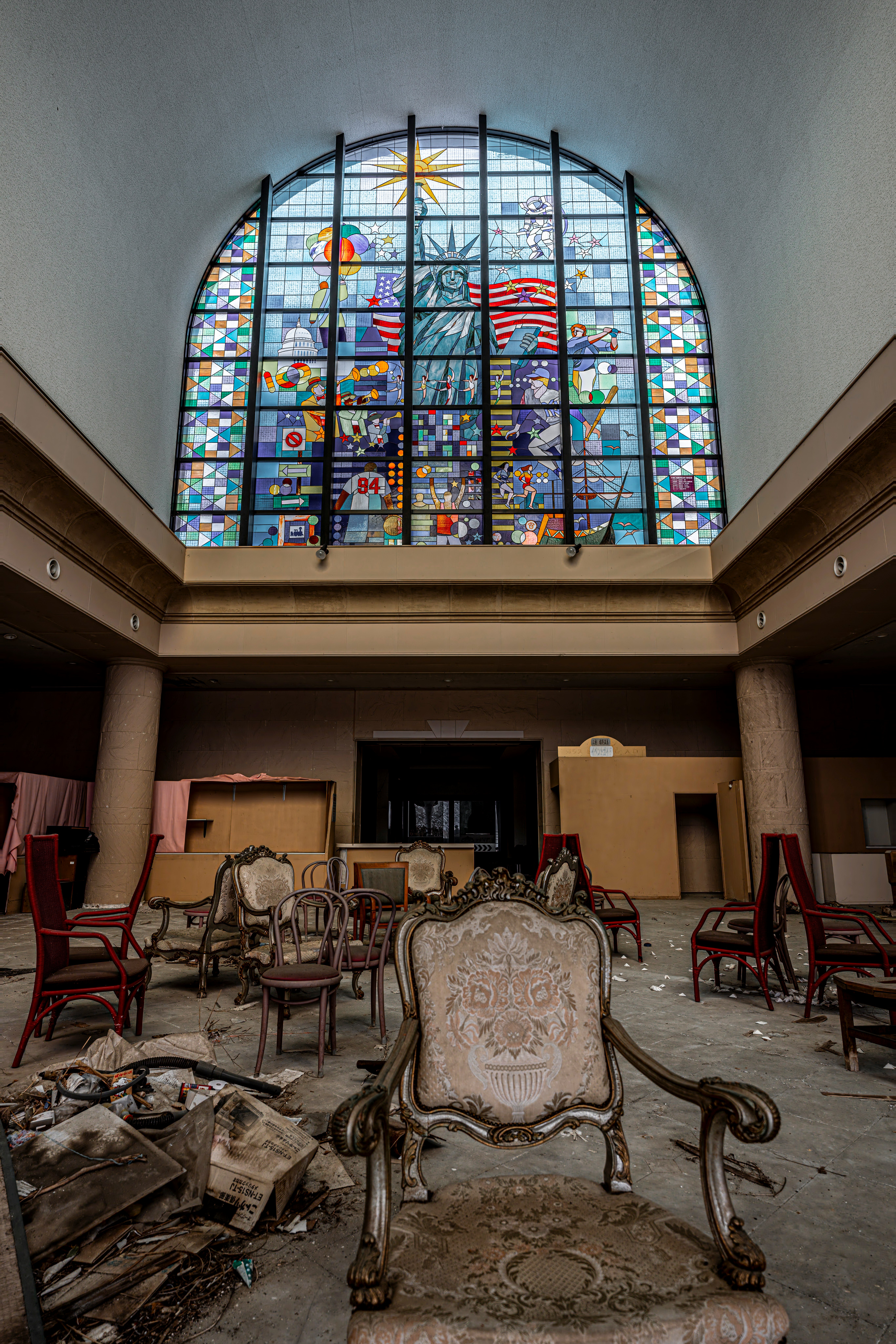 Interior bangunan terbengkalai dengan furnitur berserakan dan jendela stained glass yang pecah