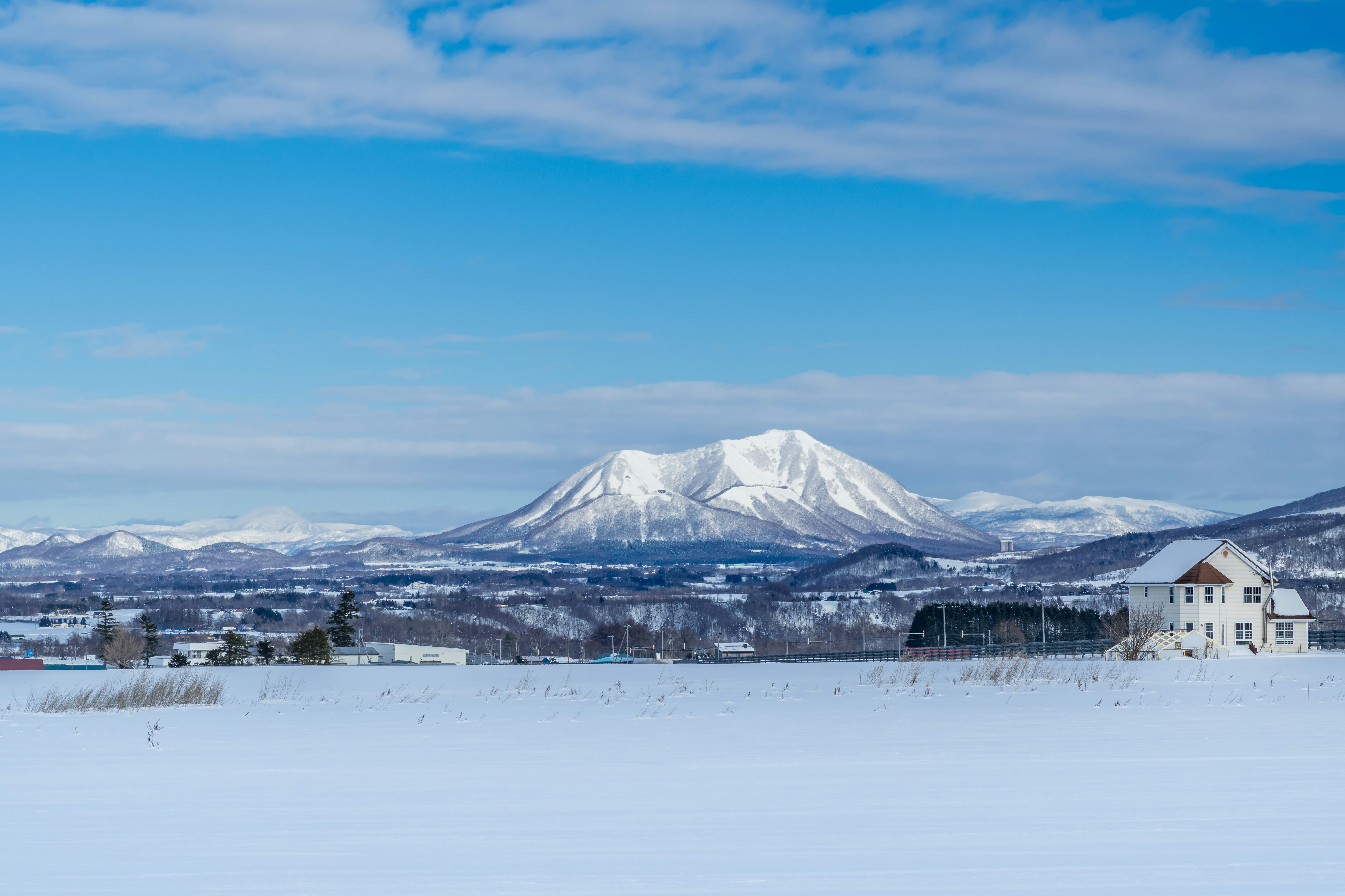 白い雪原と白い家、遠くにそびえる北海道の山並み