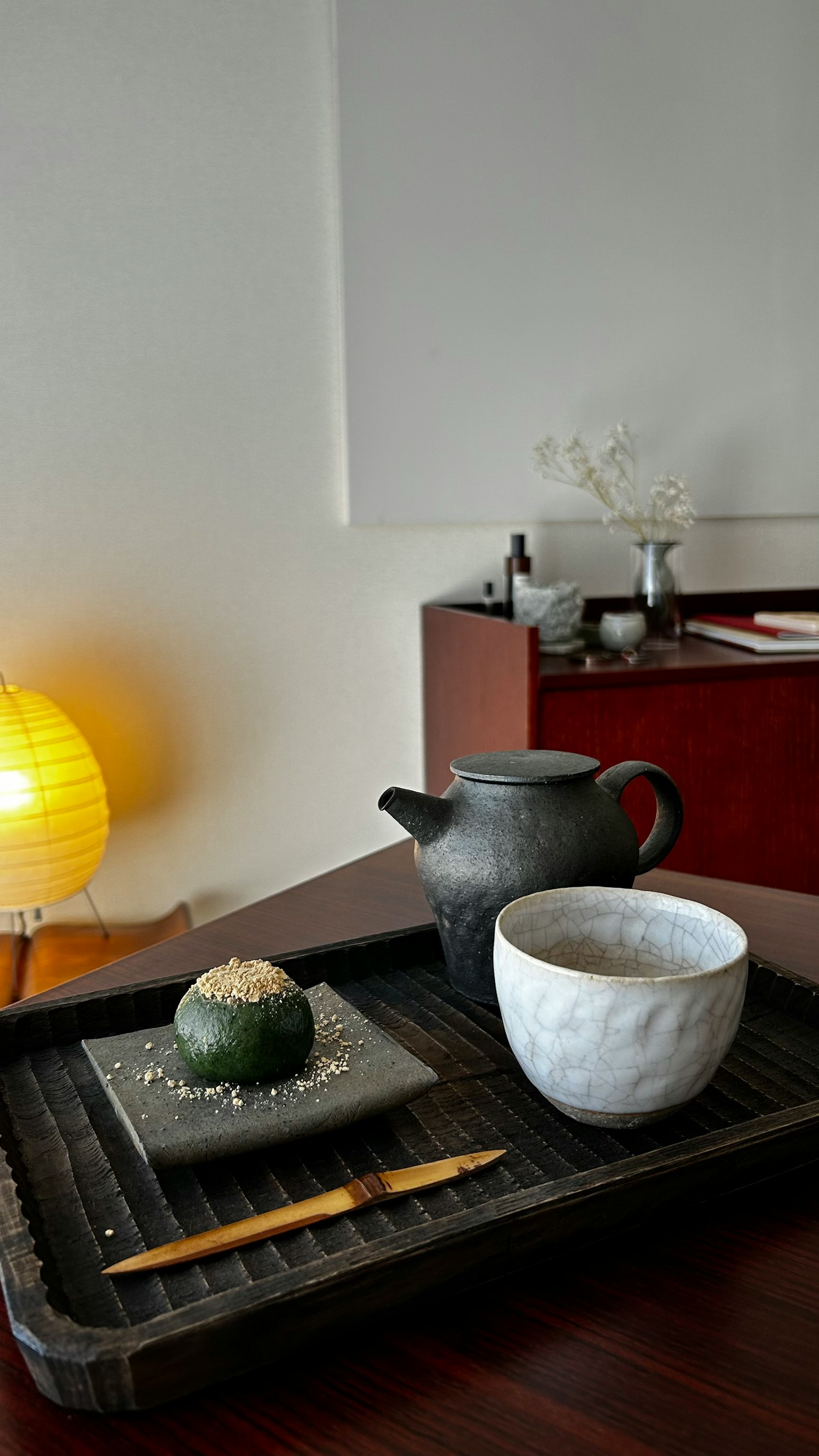 Una tetera negra y una taza blanca en una bandeja de madera con una bola de té verde decorativa