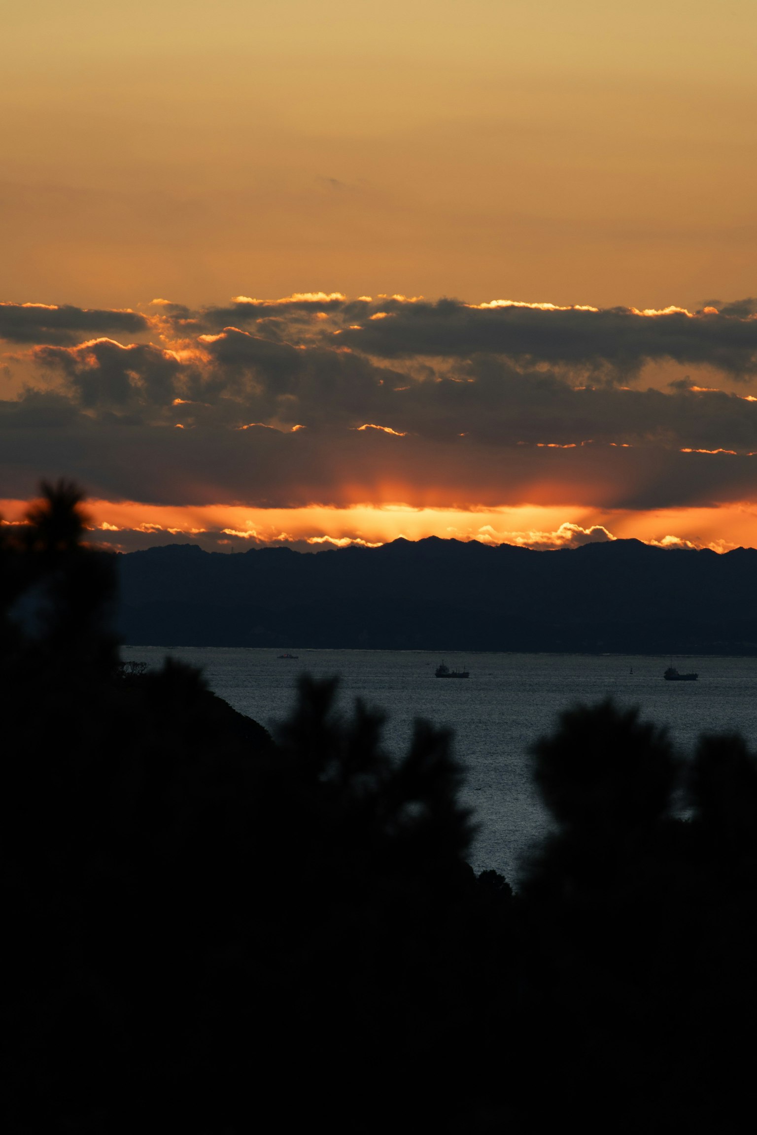 Atardecer sobre el mar con montañas al fondo y barcos a lo lejos