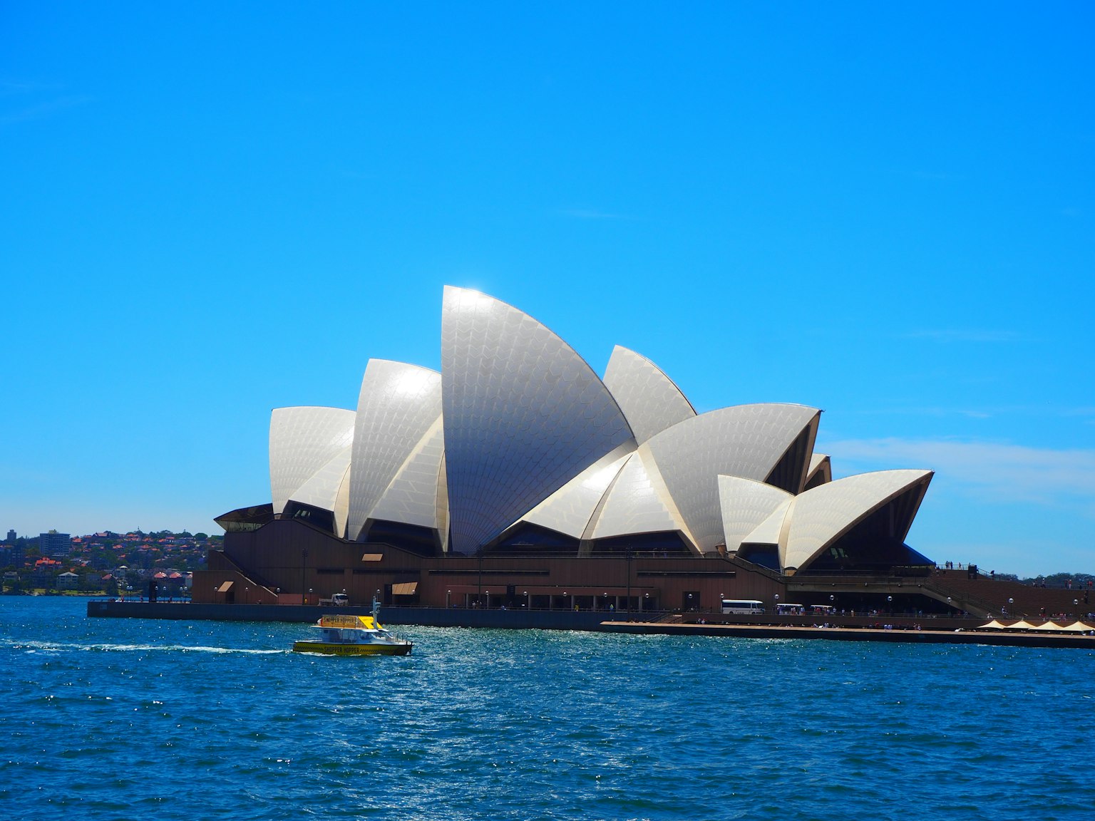 Sydney Opera House dengan arsitektur putih seperti layar di depan langit dan air biru