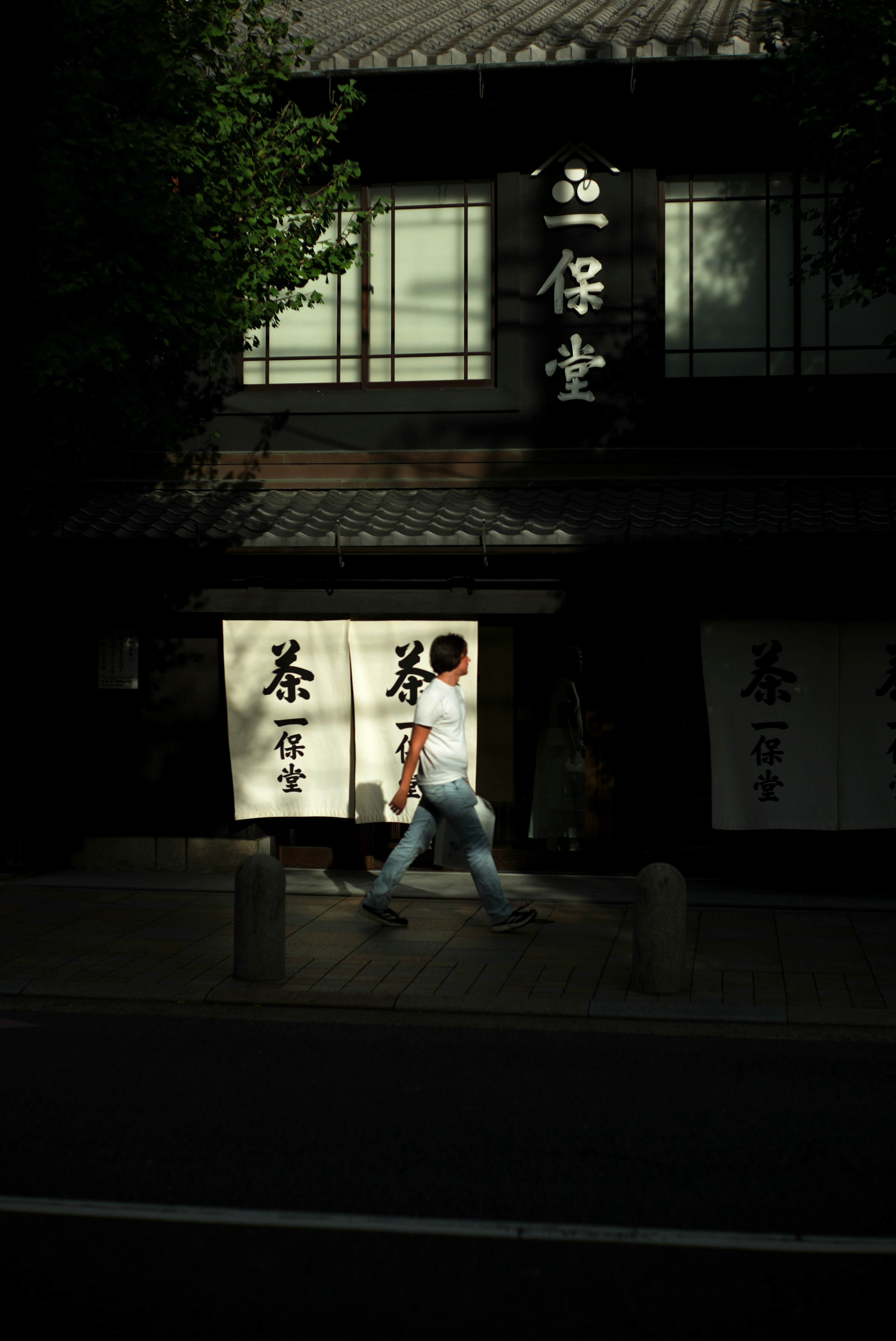 夕方の光の中で一保堂の看板前を歩く人のある路地の街並み