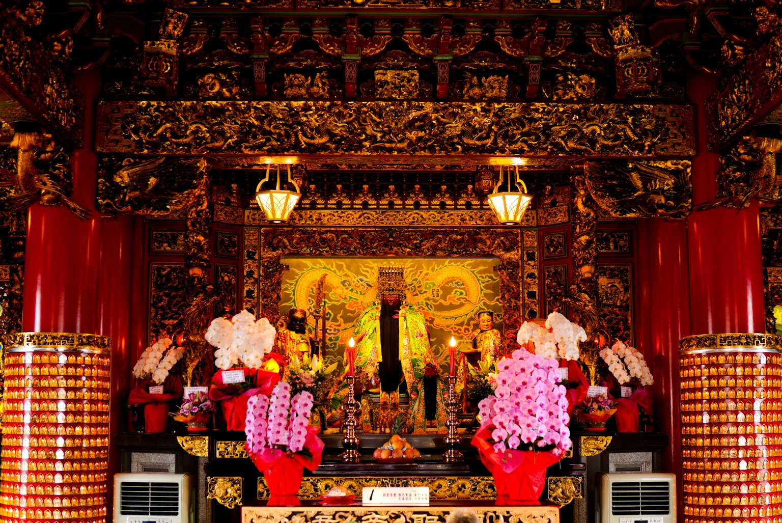 Interior of a richly decorated temple featuring a statue and colorful flowers