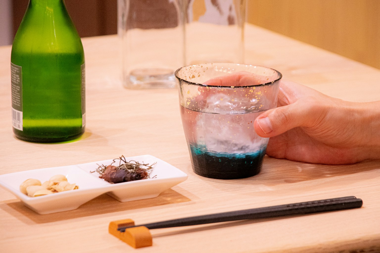 A glass with blue drink and a bottle of sake on a wooden table