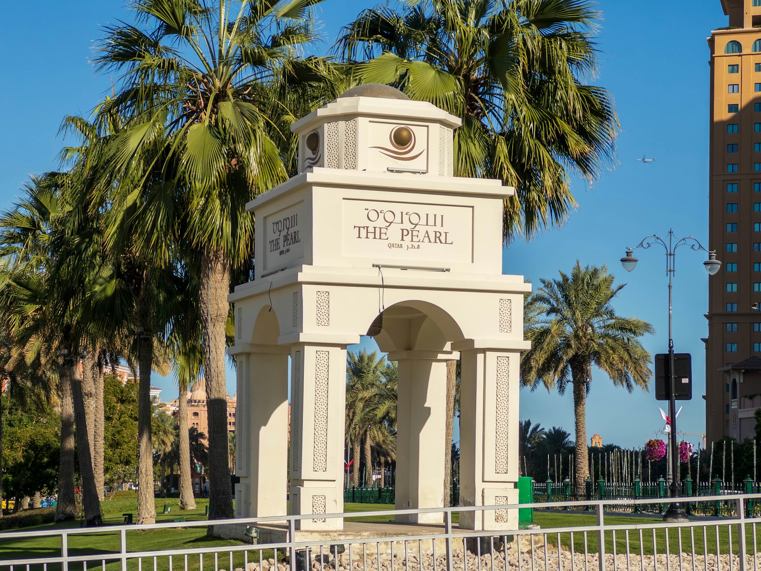 Weißes Bogenmonument umgeben von Palmen und blauem Himmel